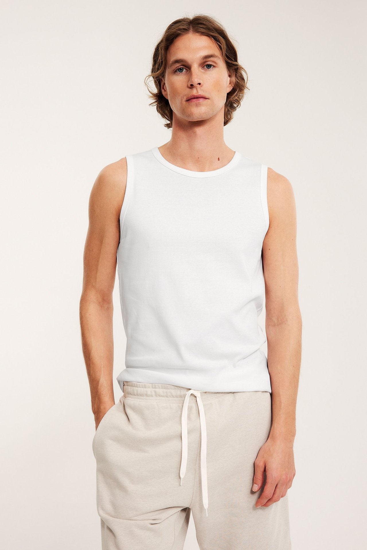 Widok z przodu mężczyzny w białym, prążkowanym bawełnianym podkoszulku i jasnobeżowych dresach.