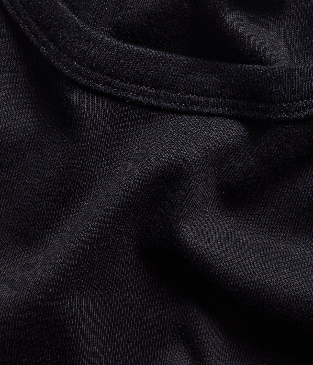 Zbliżenie czarnego topu z bawełny w prążek 1x1, ukazujące fakturę materiału i szew dekoltu.