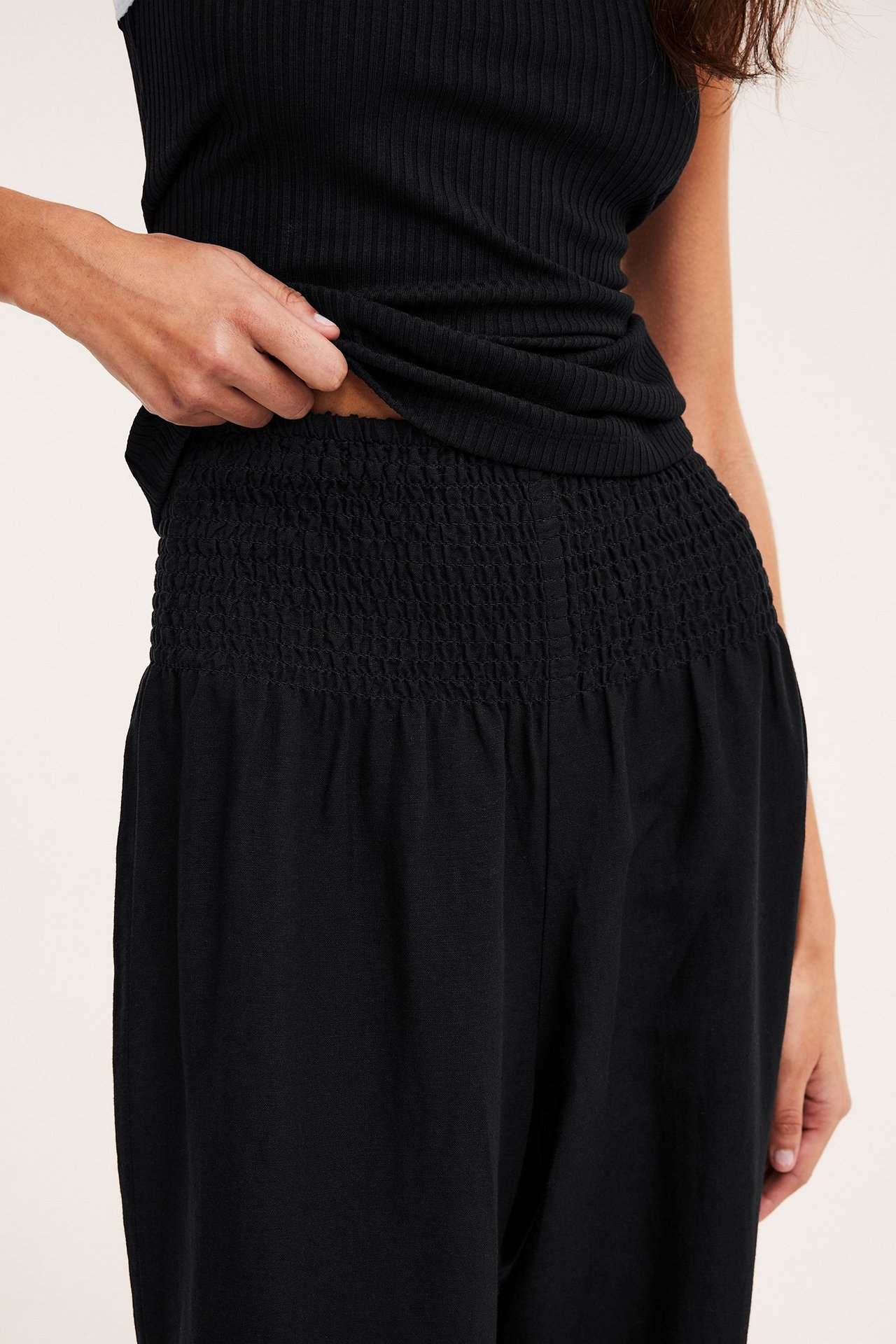 Lähikuva naisesta mustissa leveissä pellavasekoitehousuissa smock-vyötäröllä ja musta ribbitoppi.