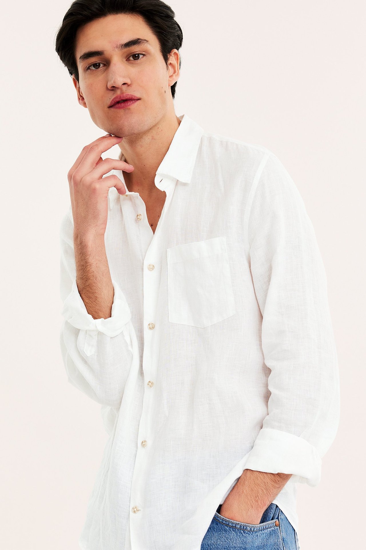 Frontvy av man i vit linneskjorta med normal passform, bröstficka, ljusa knappar och blå jeans.
