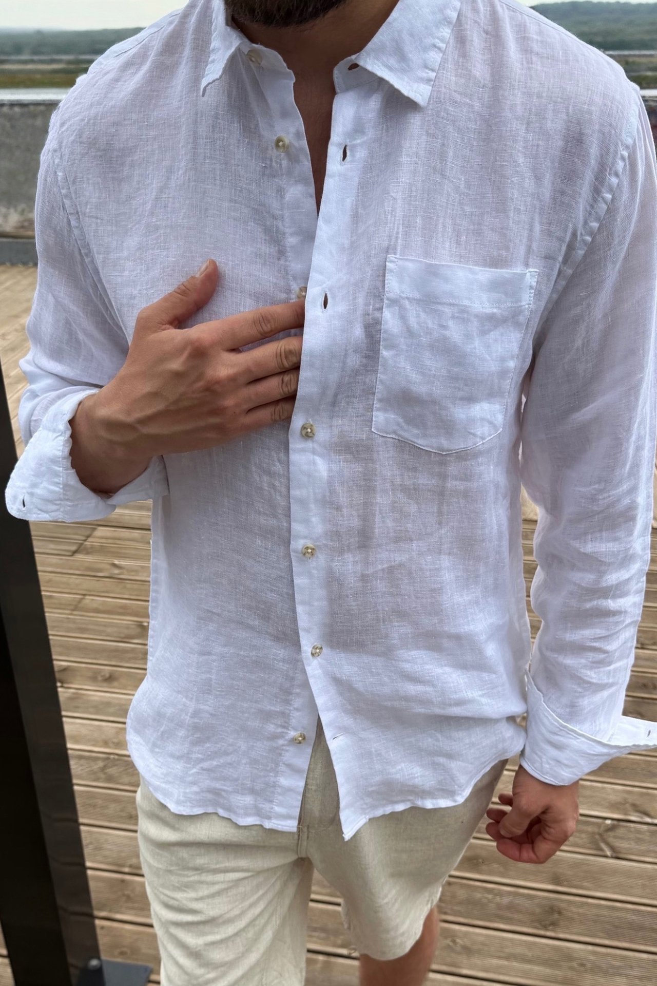Framsida: man i öppen vit linneskjorta i regular fit med bröstficka och beige shorts.