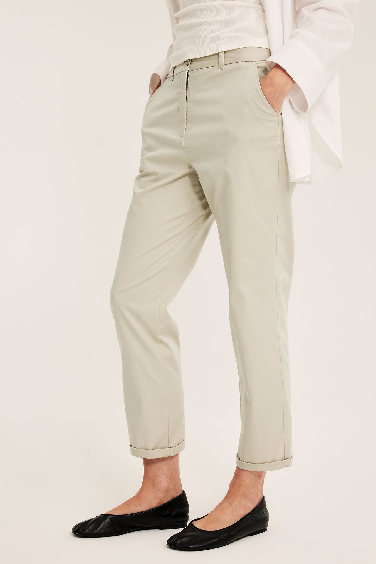 Forfra: Kvinne i offwhite chinos, hvit ribbet topp, hvit skjorte og svarte ballerinasko.