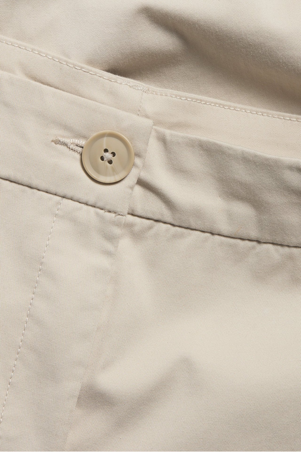 Zbliżenie beżowych bawełnianych chinosów ze stretchem, z widocznym jasnym zapięciem na guzik.