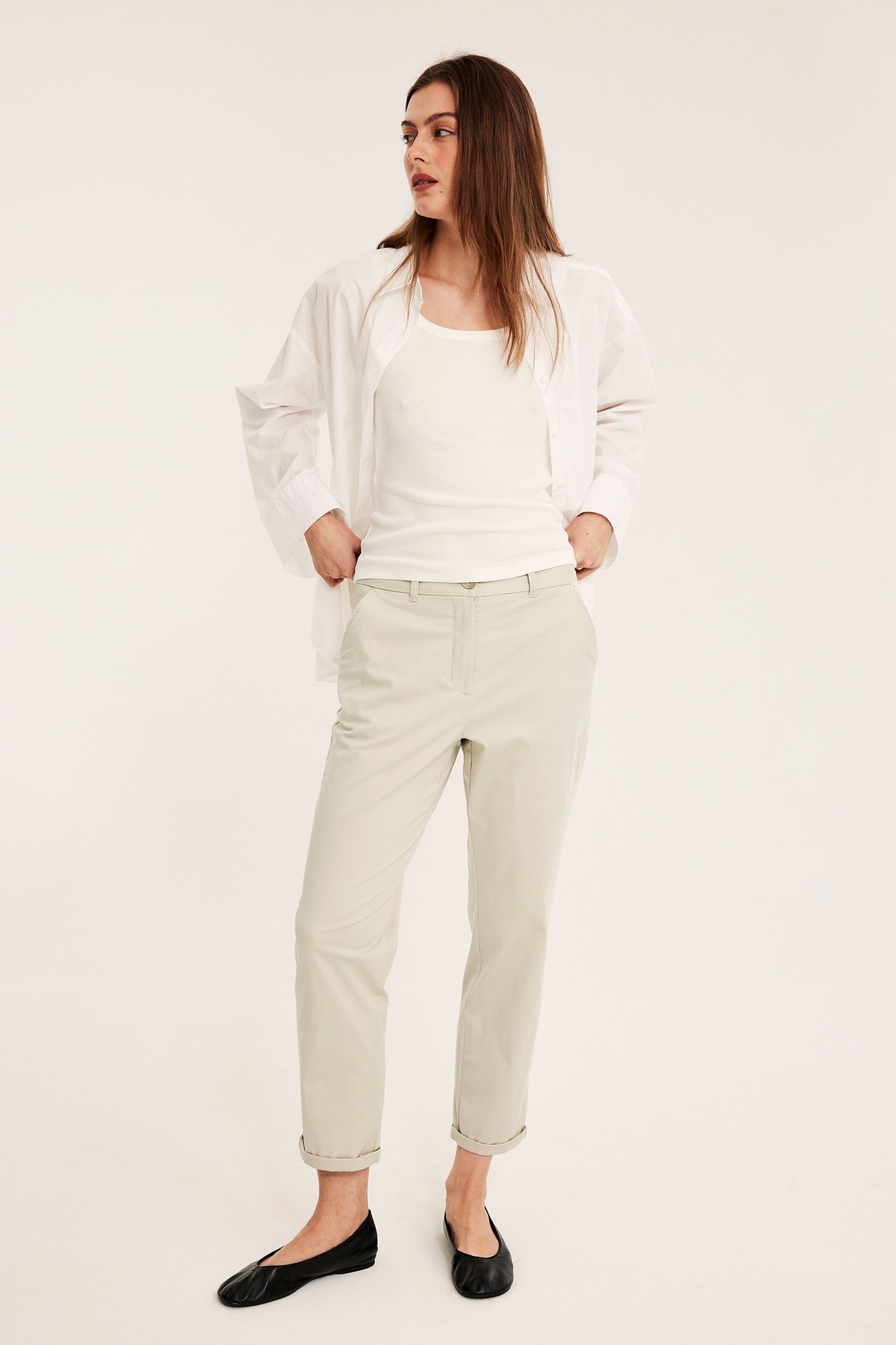 Frontvisning av kvinne i offwhite stretchchinos, hvit tanktopp, åpen hvit skjorte og svarte ballerinasko.