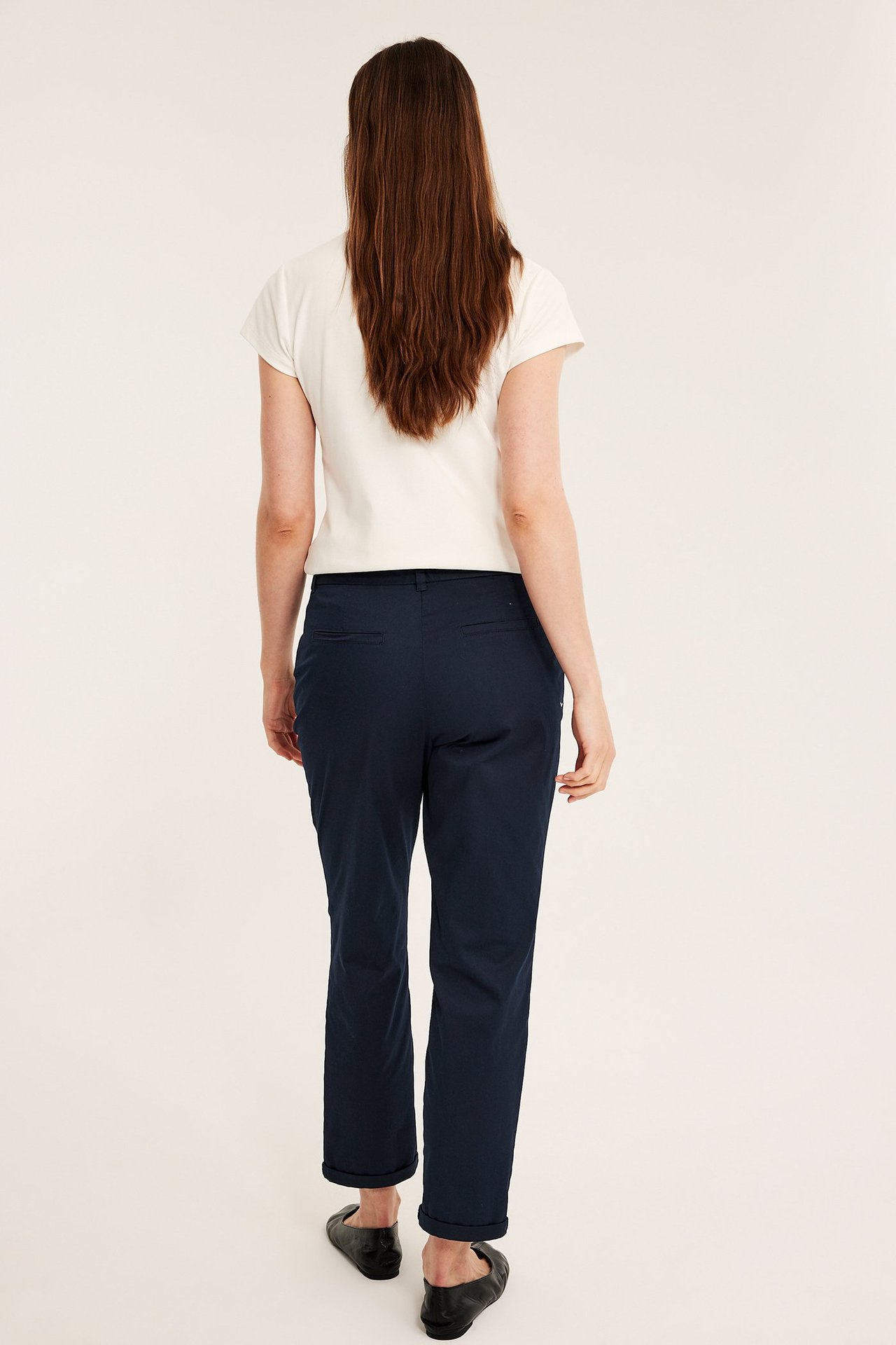 Widok z tyłu kobiety w granatowych, elastycznych spodniach chinos z twillu, beżowym topie i czarnych baletkach.