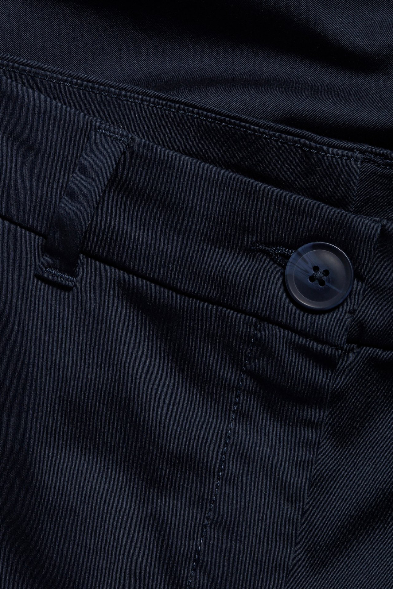 Närbild av mörkblå stretchiga bomullschinos med knapp och en bälteshälla.