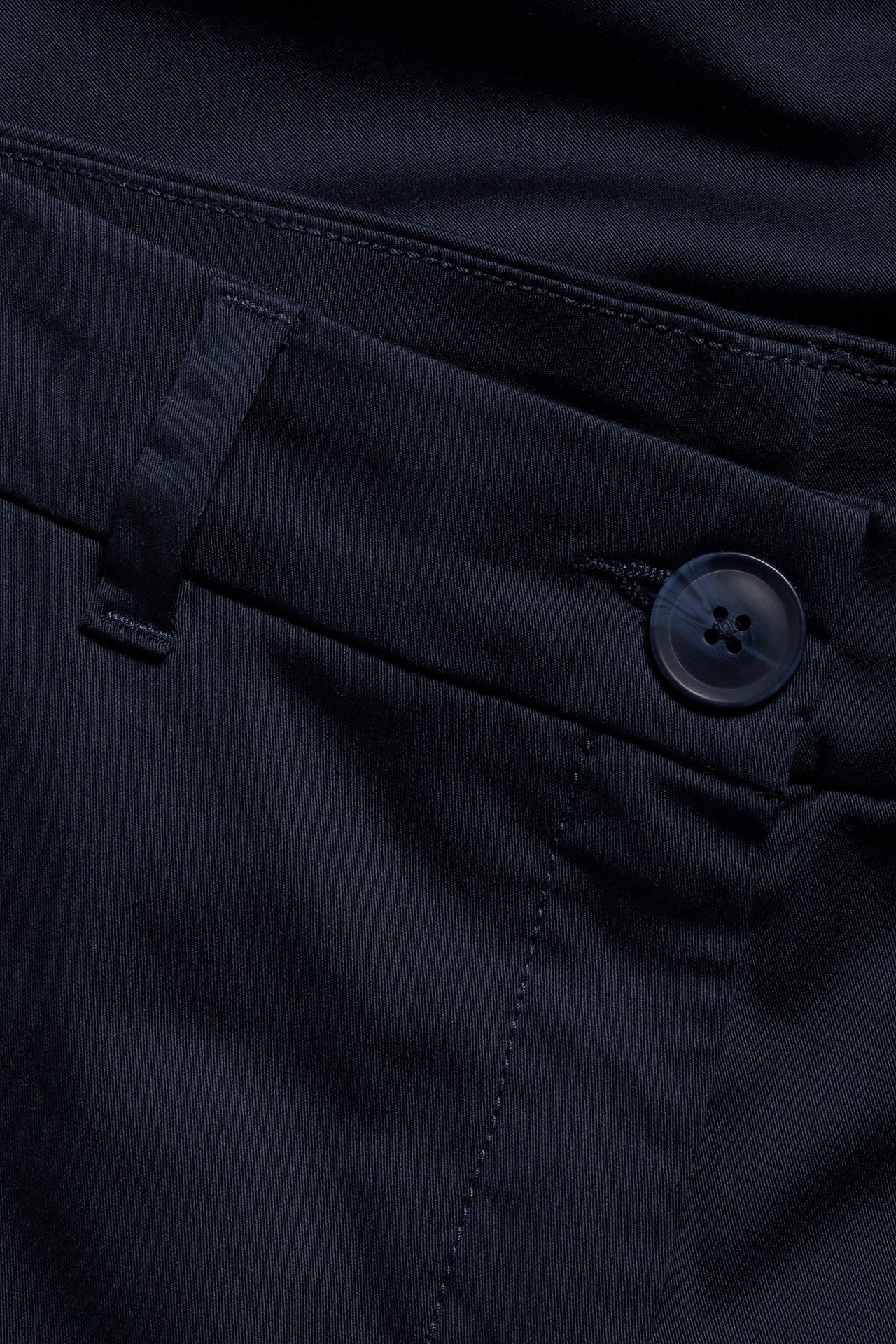 Zbliżenie na granatowe, rozciągliwe bawełniane chinosy z guzikiem i szlufką.