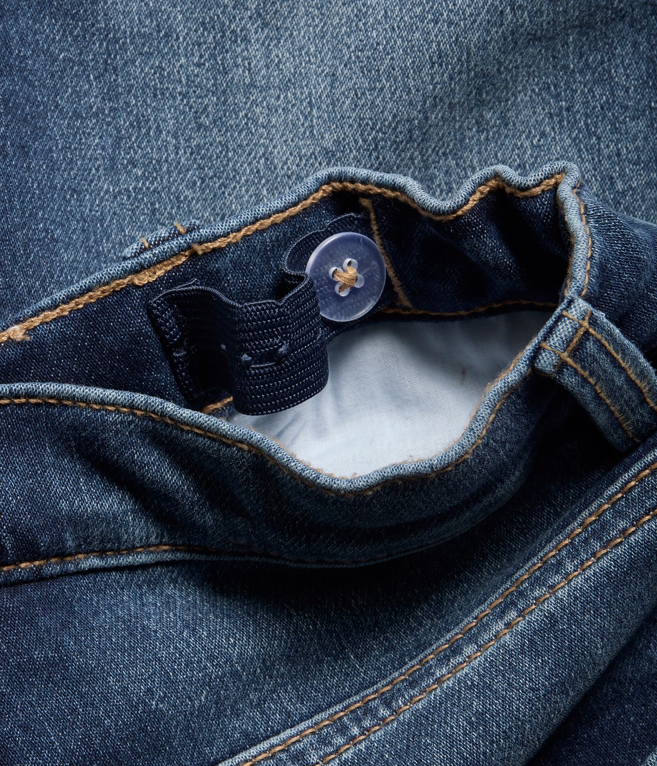Närbild av blåa denimshorts midjeband med justerbar resår och genomskinlig knapp.