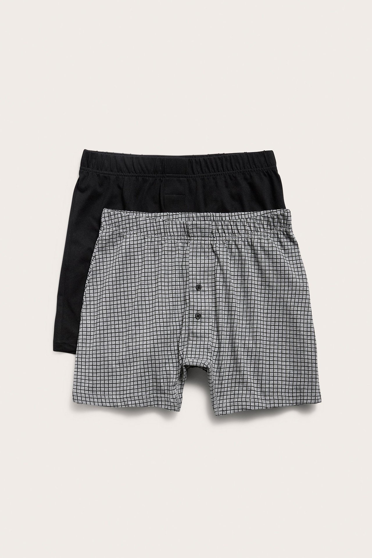 Frontvisning av mønstrede grå bomullstruser med knapper, stablet på en ensfarget svart truse.