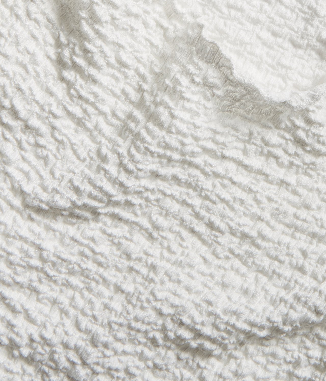 Närbild av ett offwhite texturerat åtsittande T-shirtstyg, som visar dess skrynkliga yta.