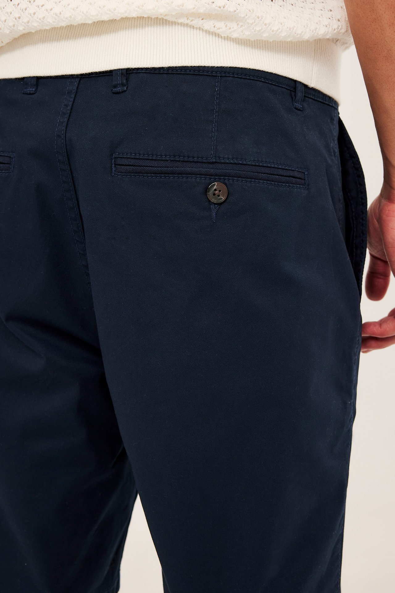 Zbliżenie, widok z tyłu: mężczyzna w granatowych bawełnianych szortach chino z kieszenią i białym swetrze.