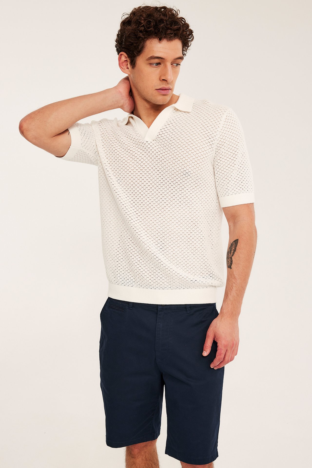 Framifrån, en man i mörkblå chinosshorts i bomullstwill och en vit stickad pikétröja.