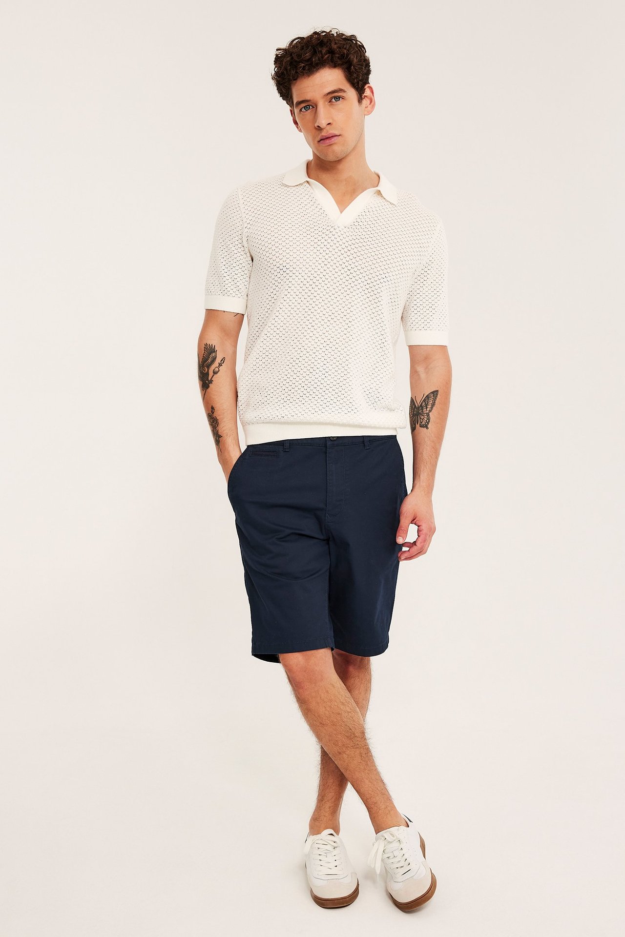Frontvy av en man i mörkblå chinosshorts, en vit stickad pikétröja och vita sneakers.