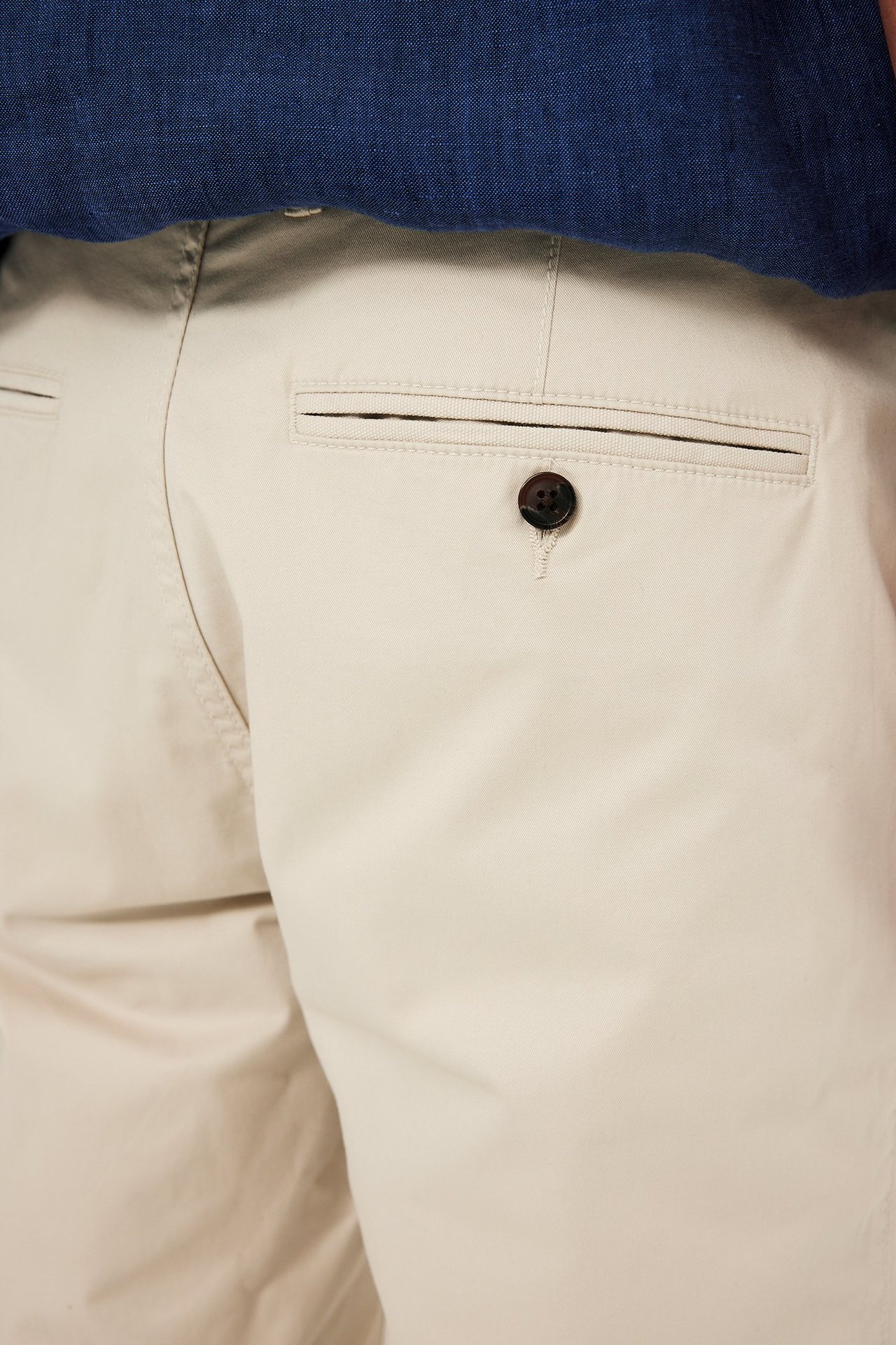 Närbild bakifrån på herrarnas ljusbeige chinosshorts i bomull med en knäppt bakficka och en mörkblå topp.