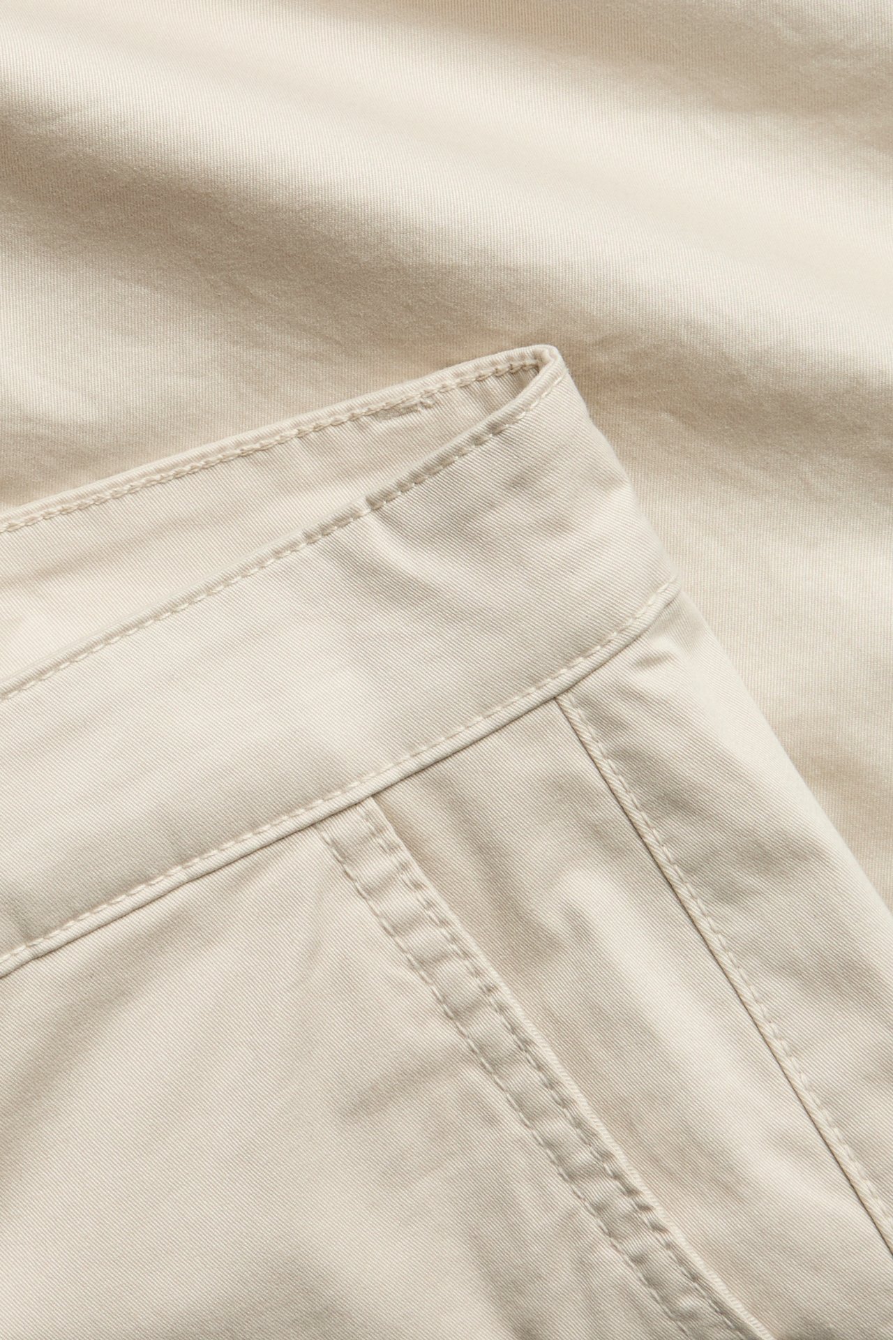 Zbliżenie na męskie jasnobeżowe szorty chino z bawełnianego twillu, widoczny pas i szwy.