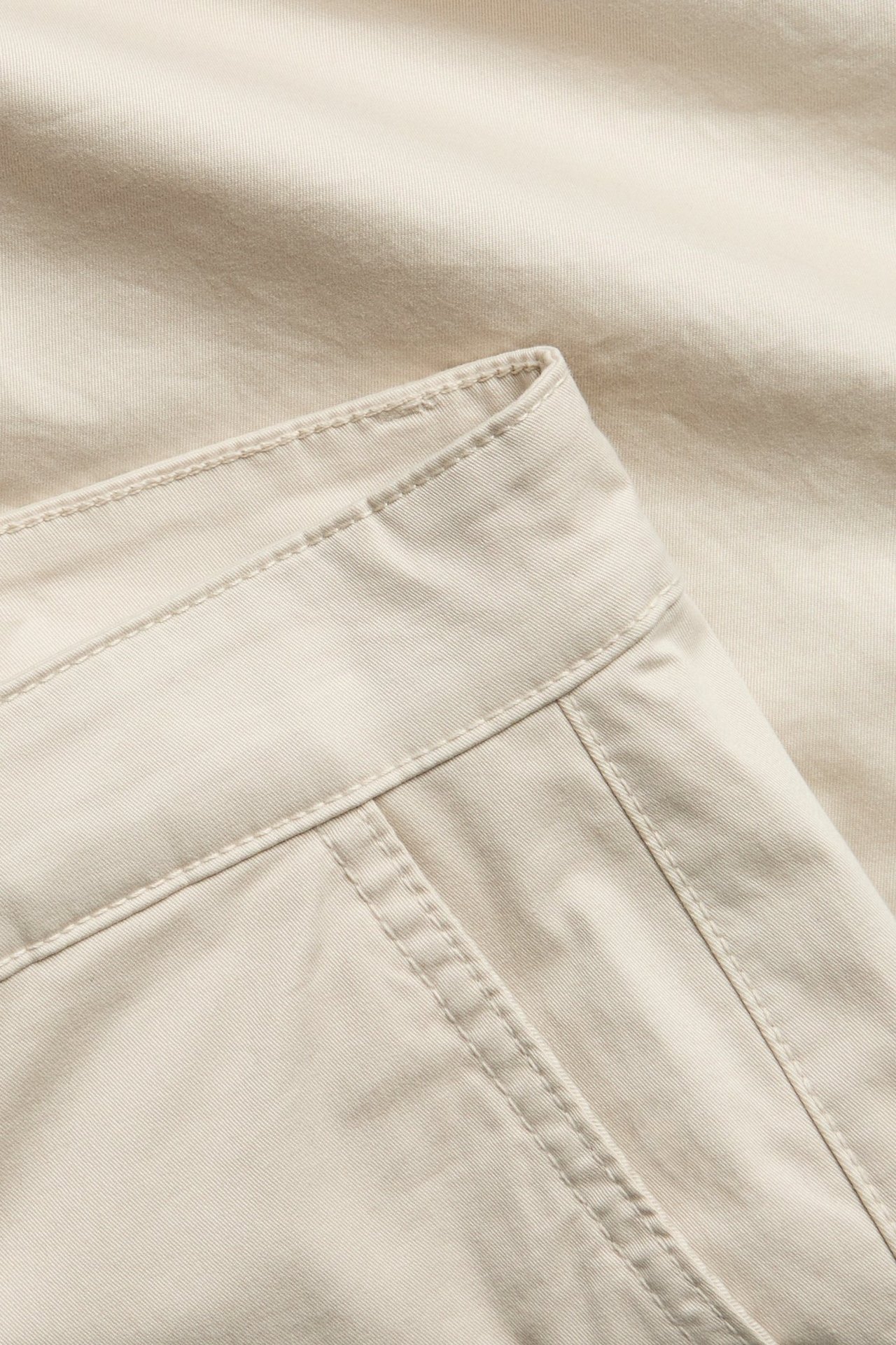 Zbliżenie na męskie jasnobeżowe szorty chino z bawełnianego twillu, widoczny pas i szwy.