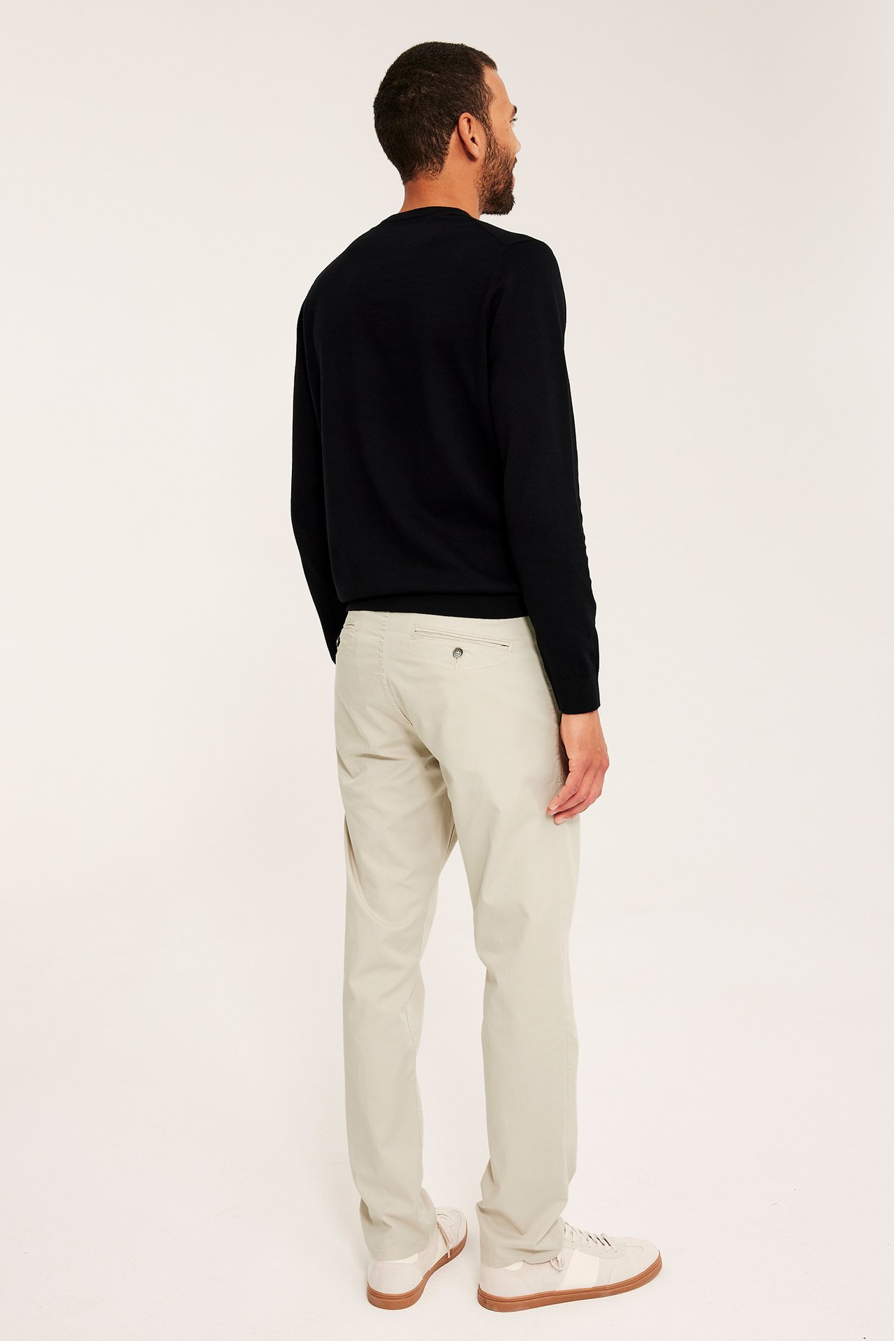 Bakfra av en mann i lysbeige regular fit chinos, en svart genser og beige sneakers.
