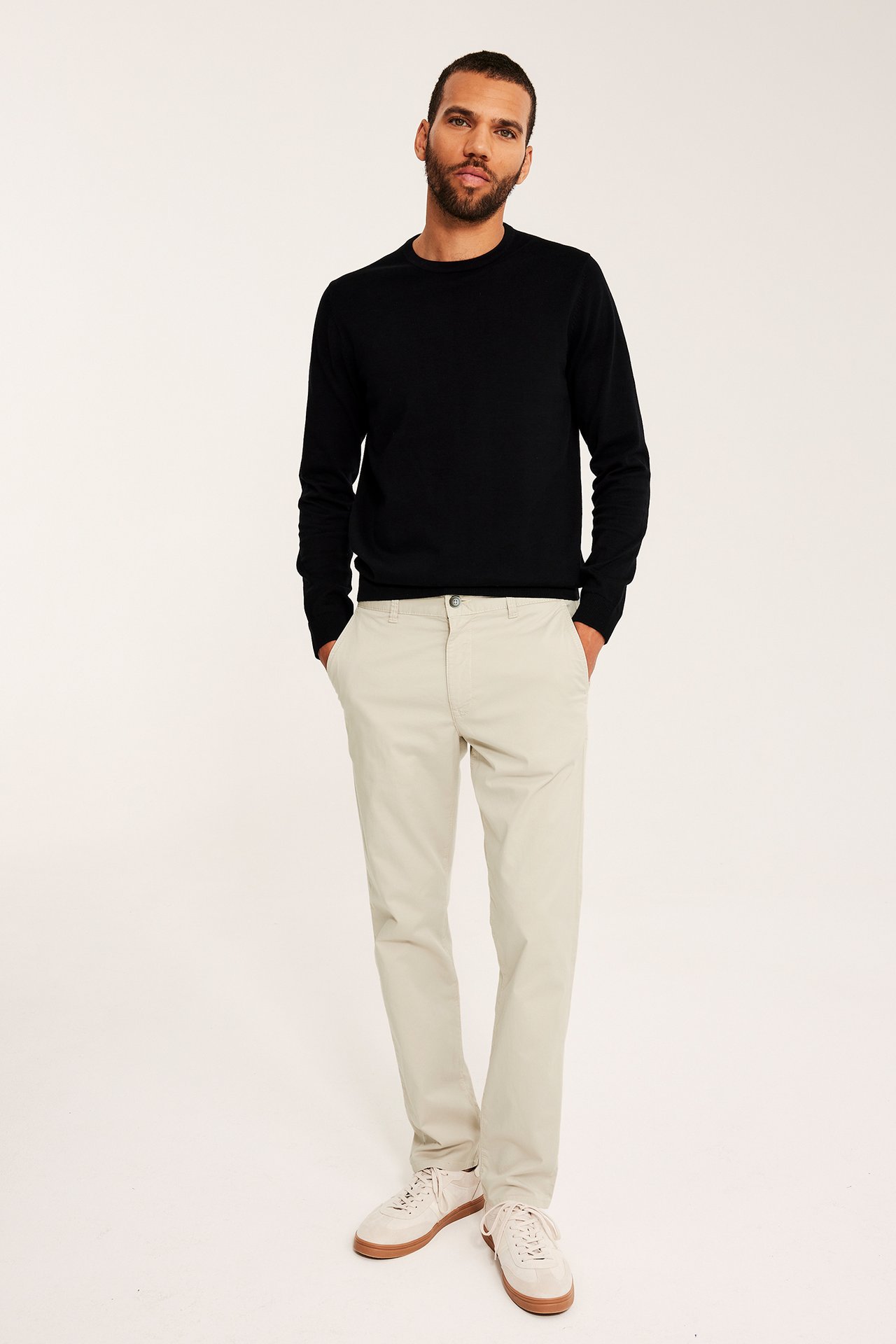 Frontutsikt av mann i lys beige regular fit bomullschinos, svart genser og lys beige joggesko.