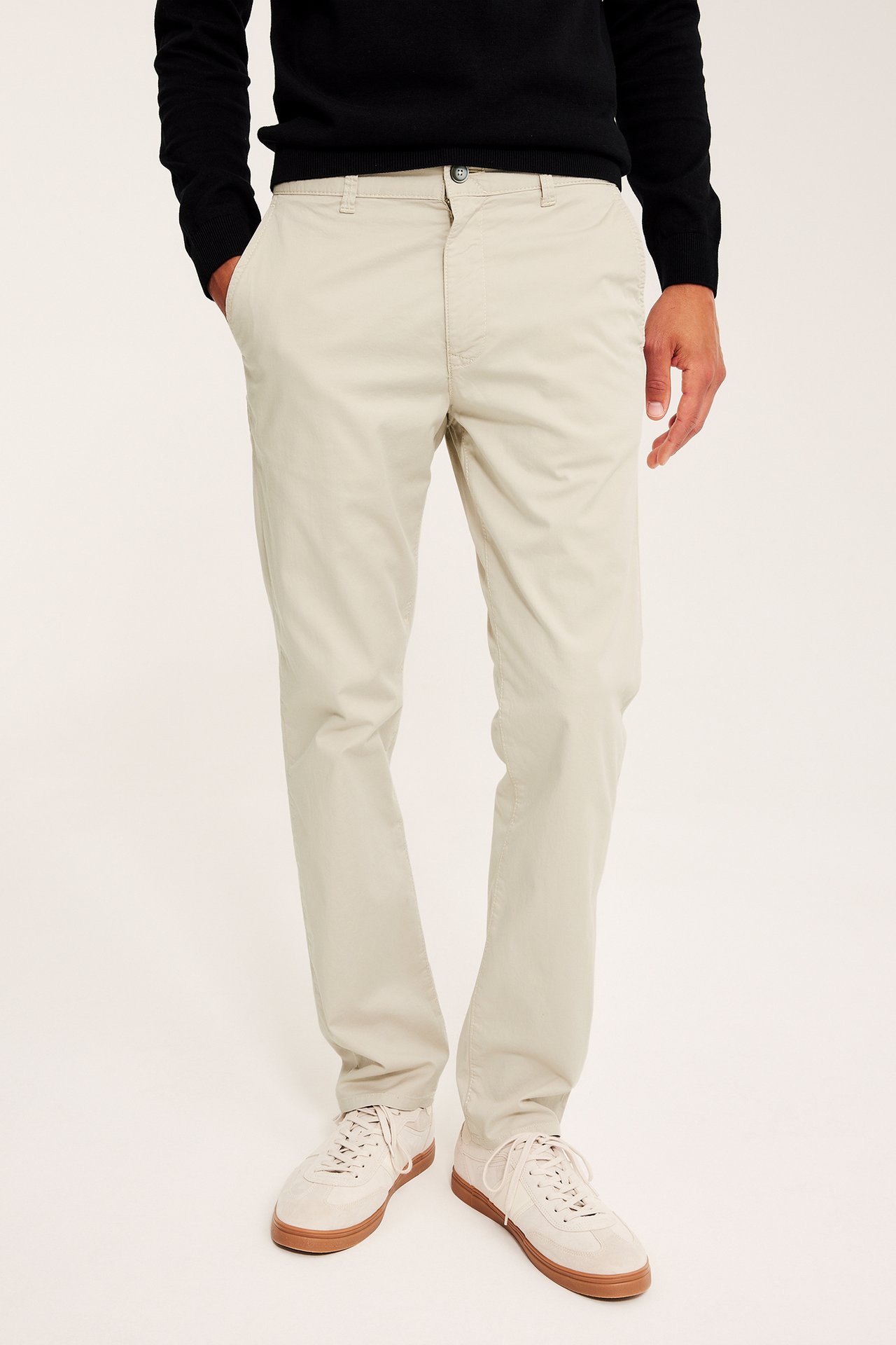 Mann forfra i lys beige regular fit stretch-bomullschinos, svart genser og lysebeige sneakers.