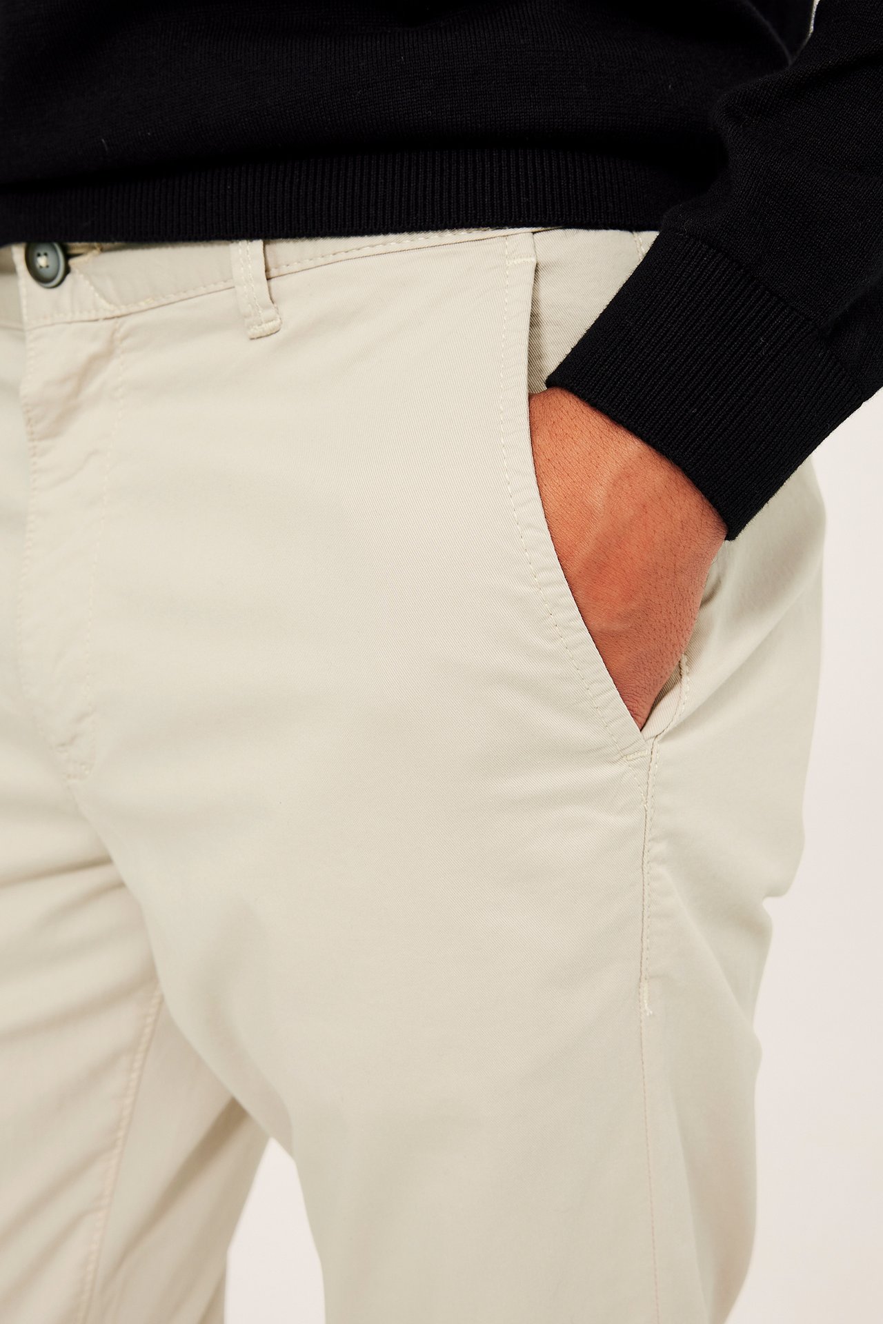 Nærbilde forfra av lysebeige regular fit bomullschinos for herre, hånd i lommen, med svart genser.