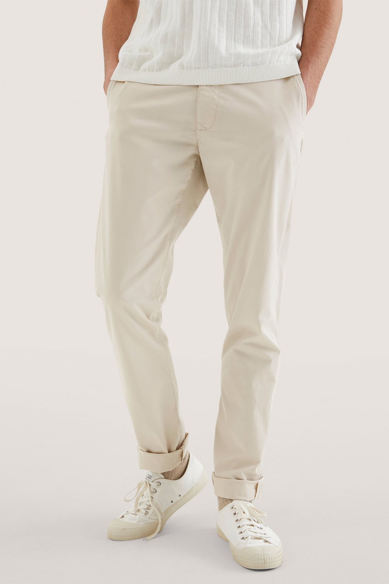 Edestäpäin: mies yllään vaaleanbeiget suorat puuvillachinot, valkoinen ribbitoppi ja valkoiset tennarit.