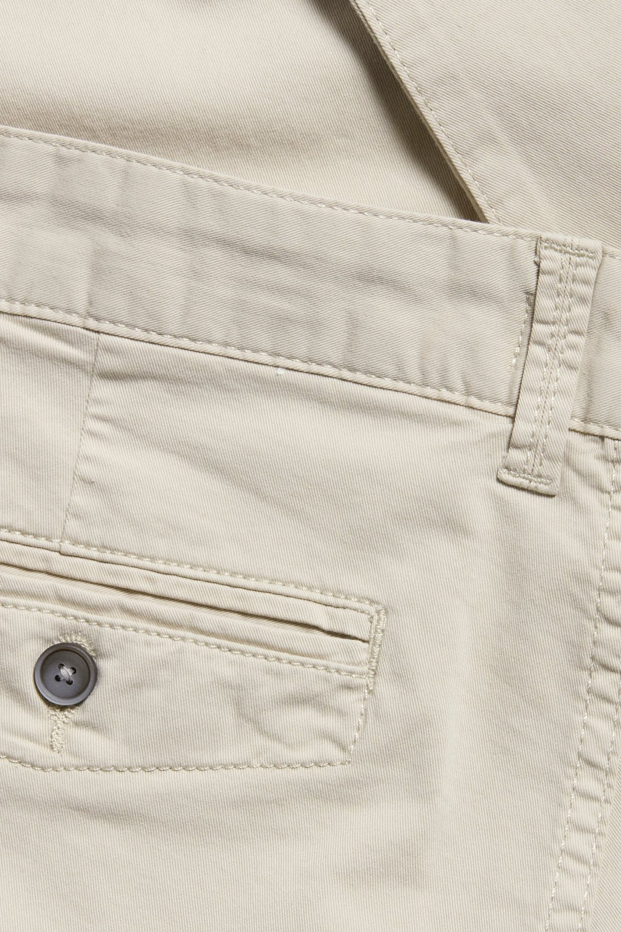 Zbliżenie na męskie jasnobeżowe chinosy bawełniane z pasem i tylną kieszenią na guzik.