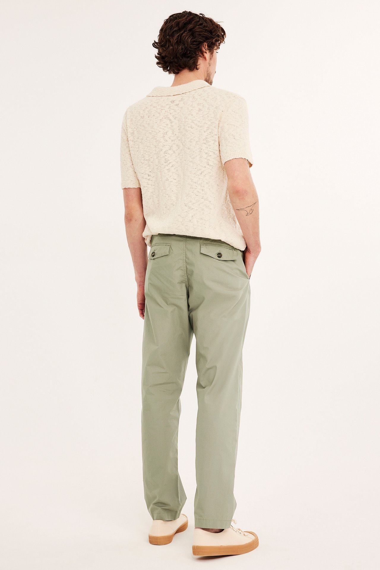 Bakifrån, man i gröna chinos med bakfickor, en ljusbeige texturerad pikétröja och beiga sneakers.