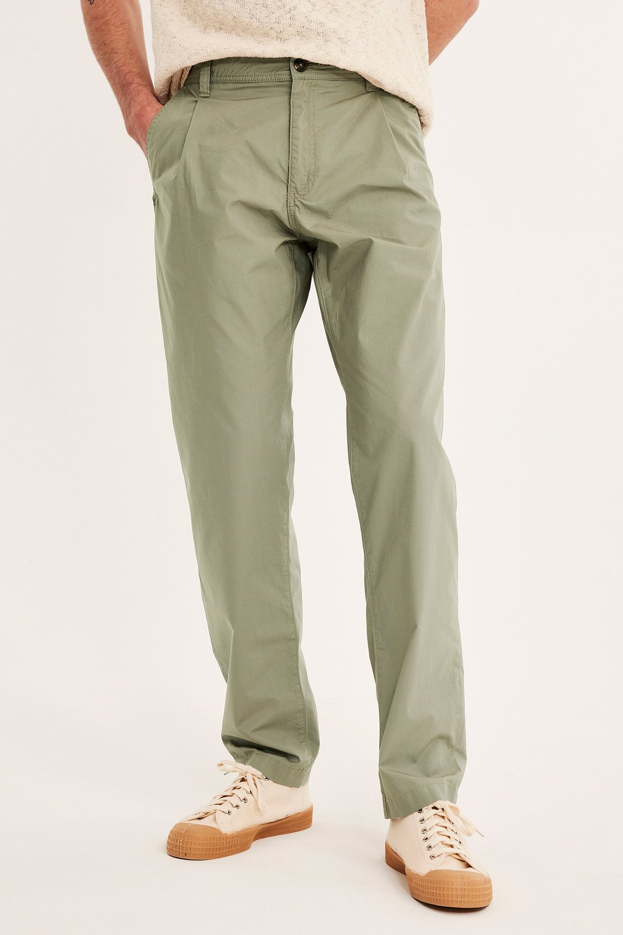 Edestäpäin, mies yllään vihreät laskostetut chinot, kermanvärinen neuletoppi ja beiget kangaskengät.