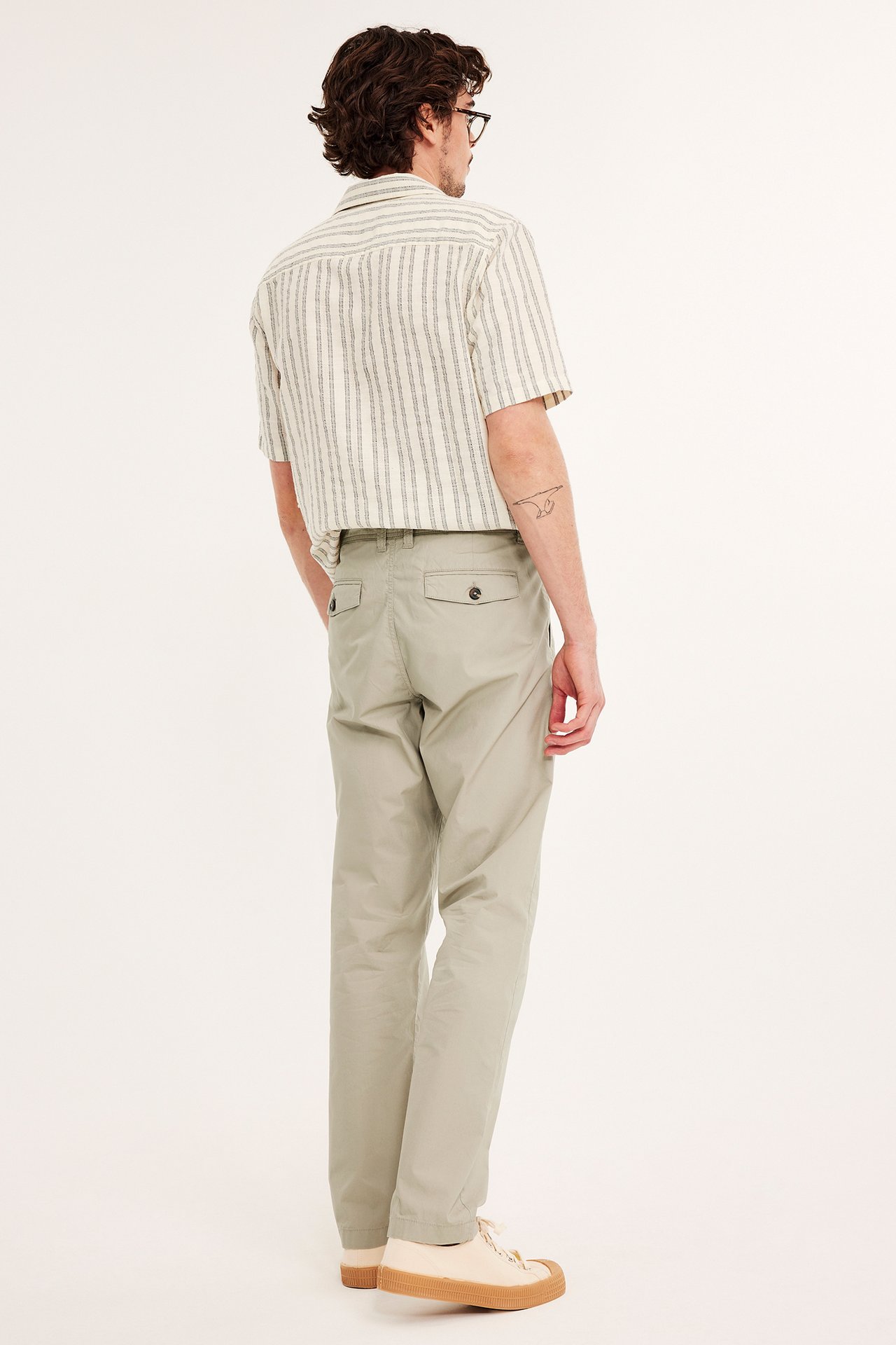 Bakifrån: man i beiga linnechinos, randig kortärmad skjorta och ljusa sneakers.