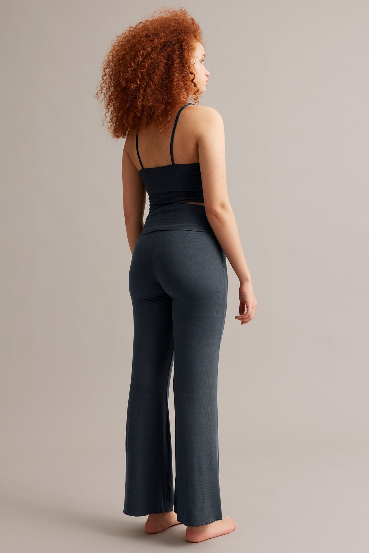 Bakre høyre visning av en kvinne i mørkeblå viskose bootcut-joggebukser og matchende camisole-topp.