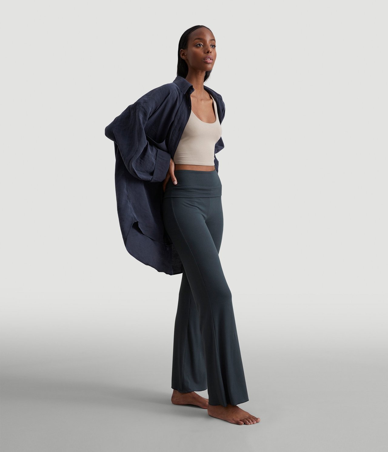 Sivukuva naisesta yllään tummansiniset bootcut-collegehousut, beige crop top ja avoin tummansininen paita.