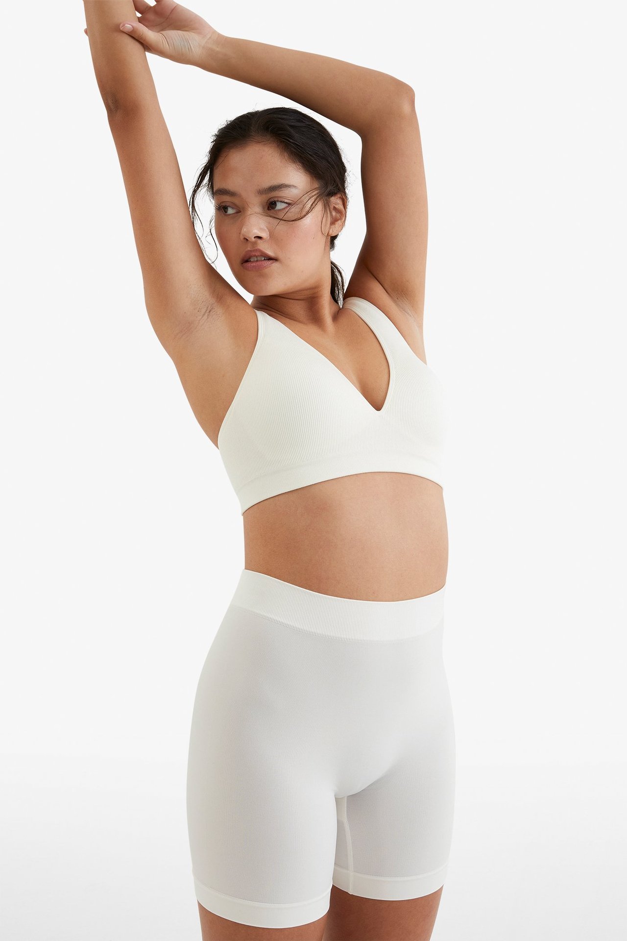 Forfra, kvinne i hvite sømløse high-waist shorts og en hvit ribbet V-hals BH.
