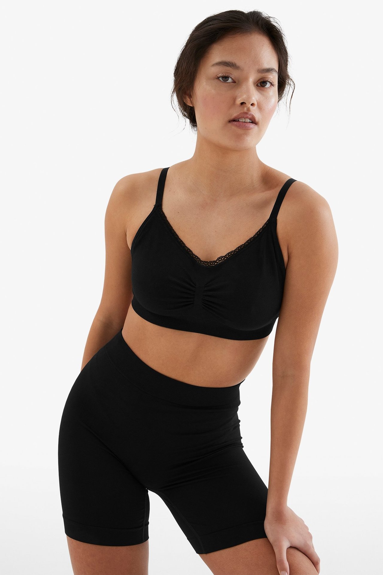 Forfra, kvinne i svarte sømløse shorts med høy midje og matchende svart bralette med blondekant.