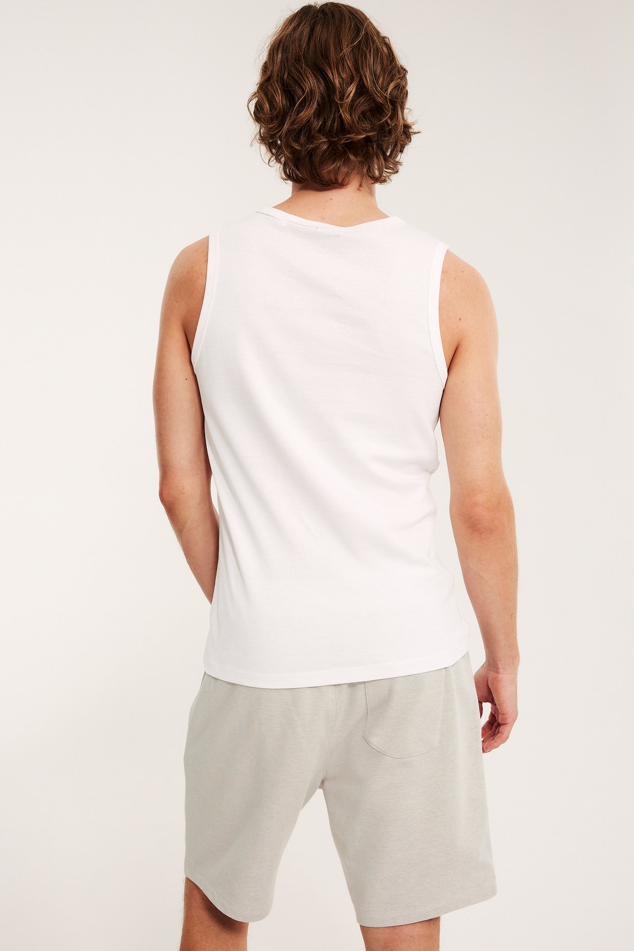 Widok z tyłu mężczyzny w beżowych melanżowych szortach dresowych z kieszenią i białym podkoszulku.