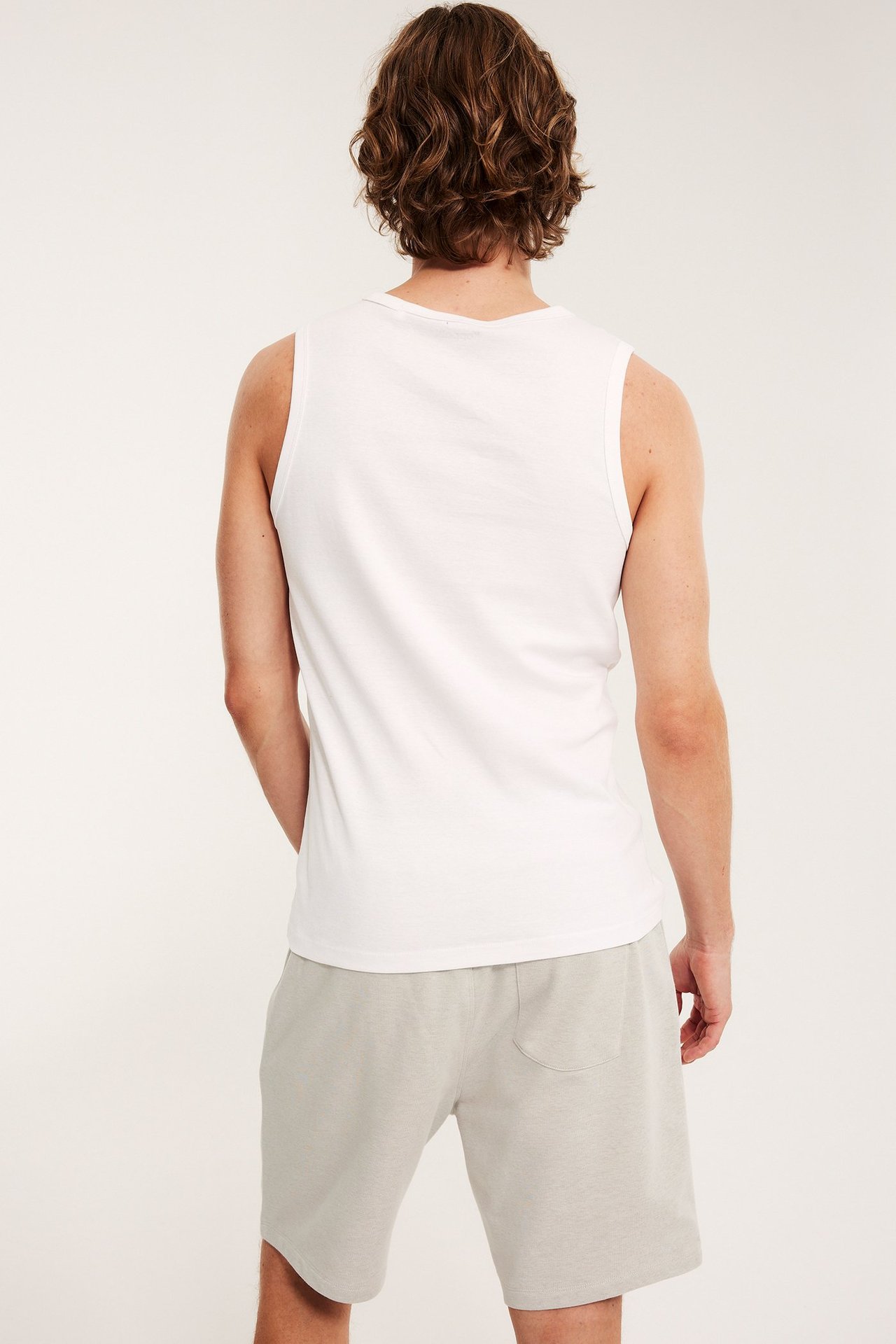 Widok z tyłu mężczyzny w beżowych melanżowych szortach dresowych z kieszenią i białym podkoszulku.