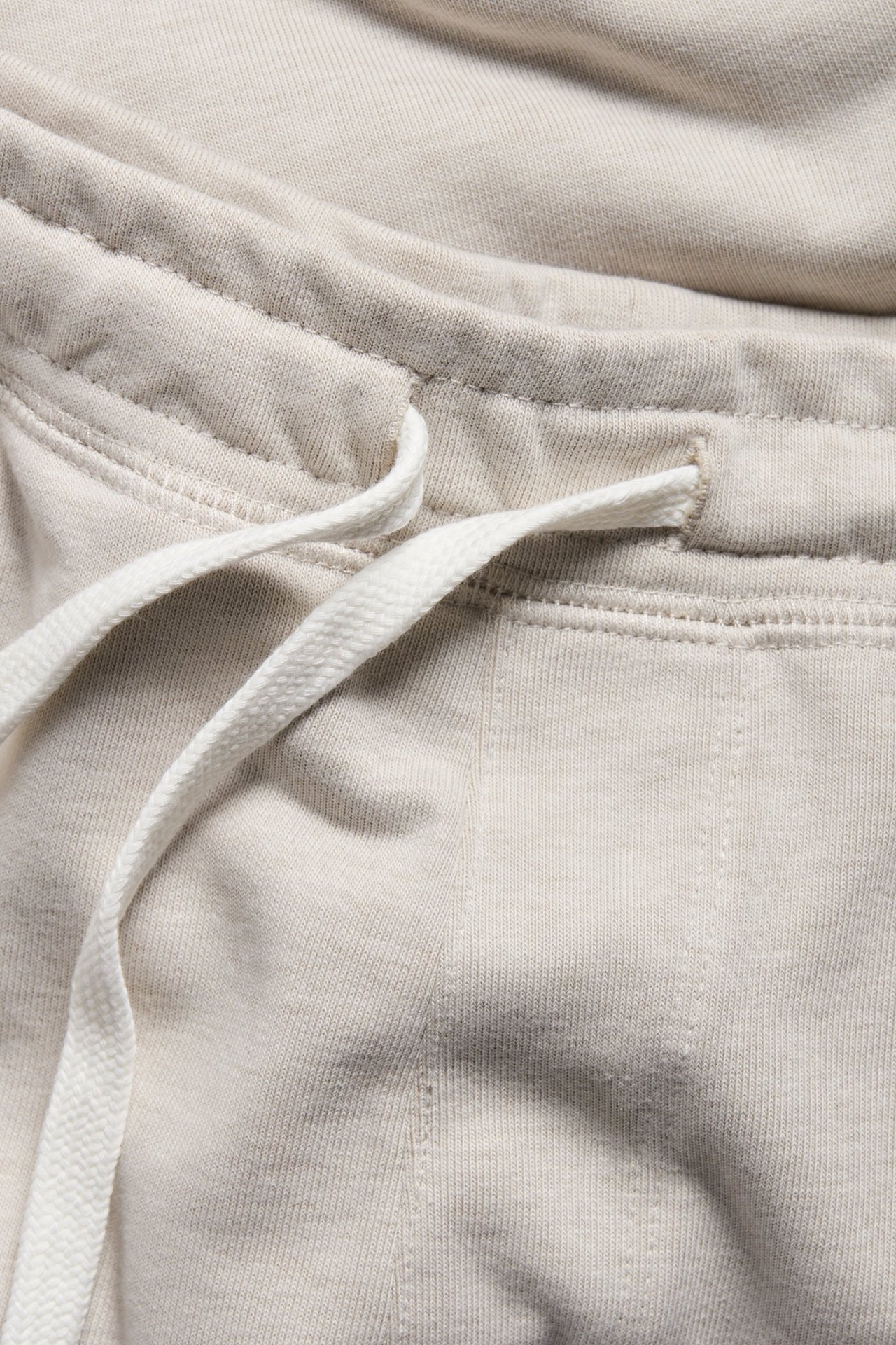 Zbliżenie beżowych melanżowych męskich szortów dresowych z elastyczną talią i białym sznurkiem.
