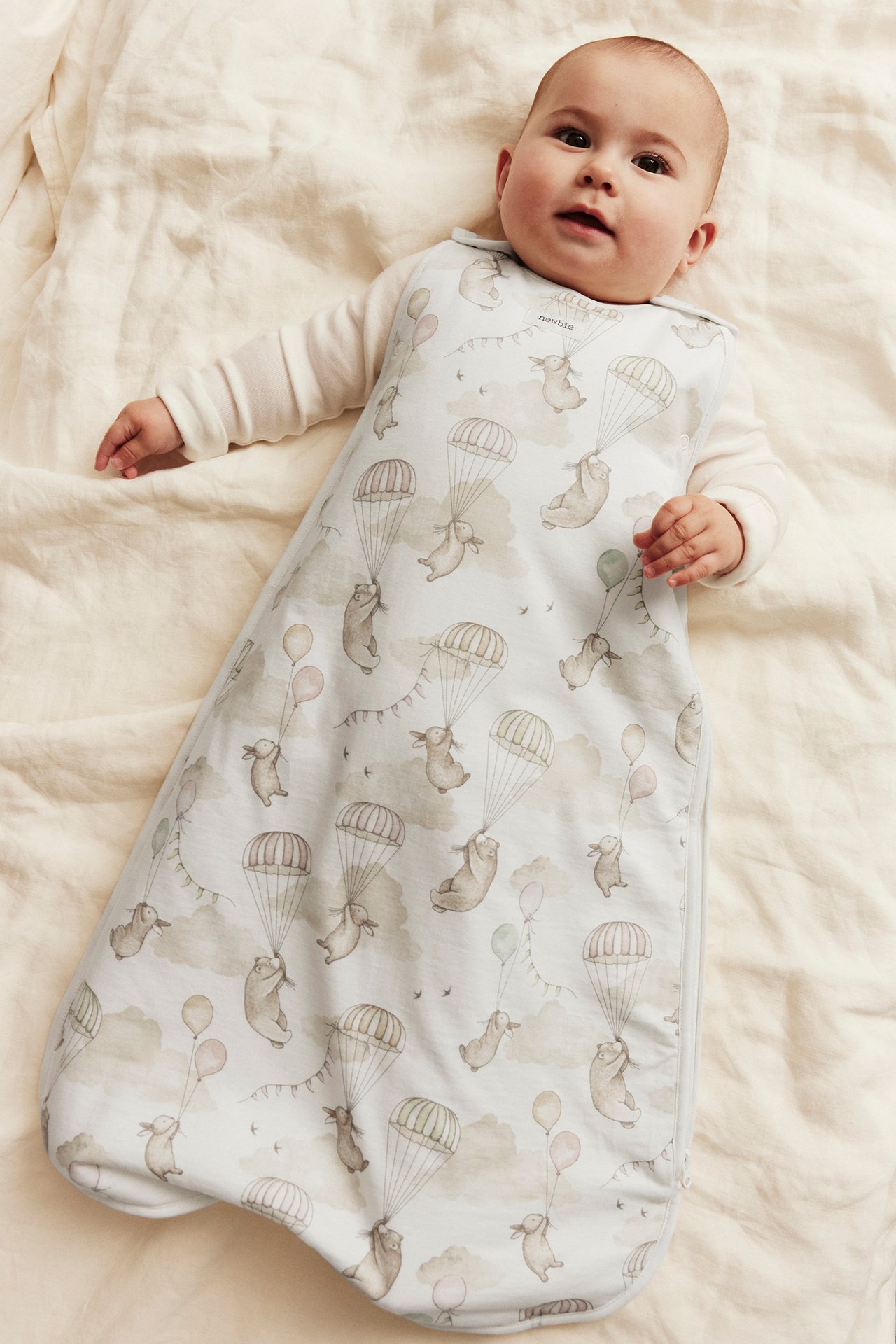 Oversikt over en baby i en mønstret lyseblå kaninsovepose og hvit body.