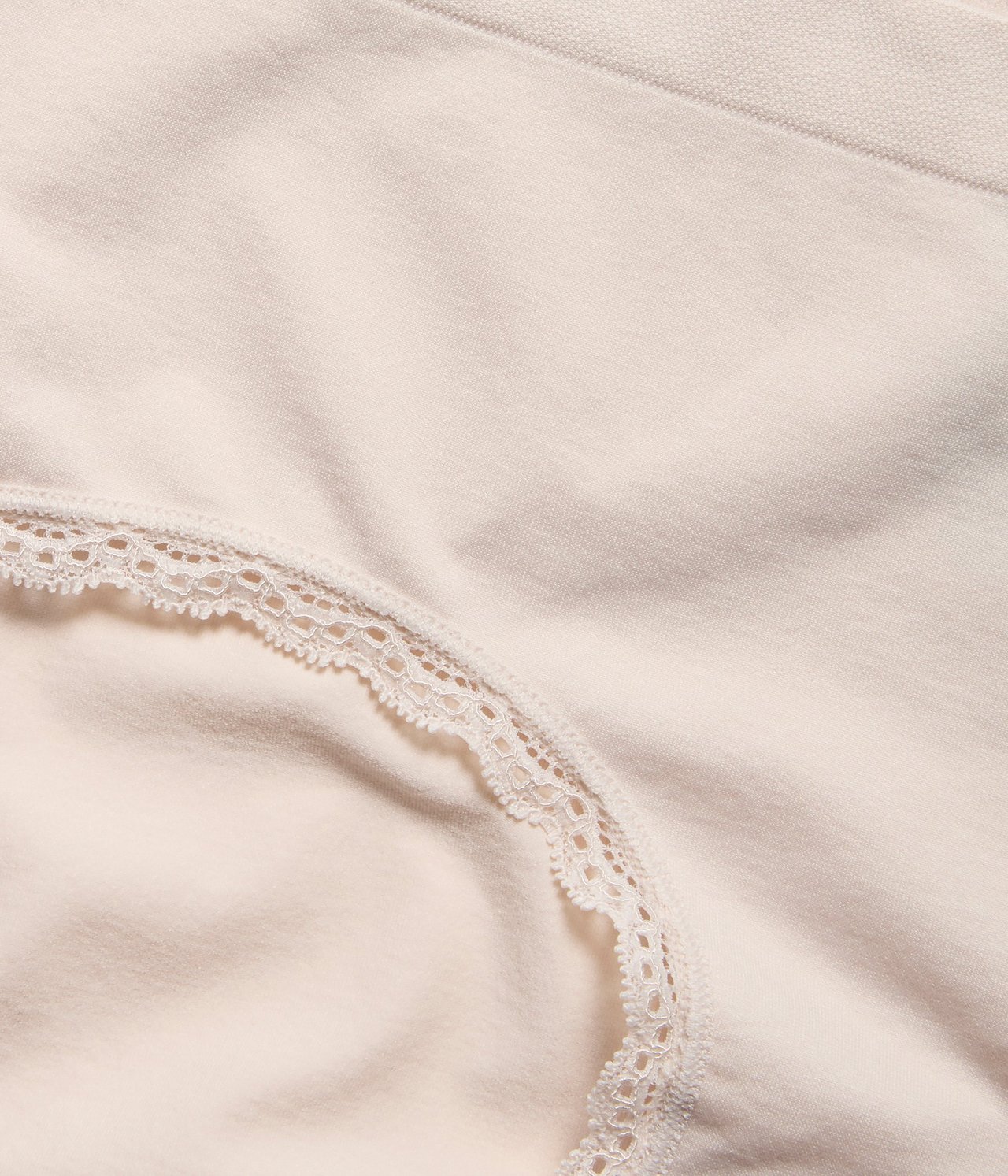 Zbliżenie na jasnobeżowe bezszwowe figi typu hipster z delikatną koronkową lamówką.