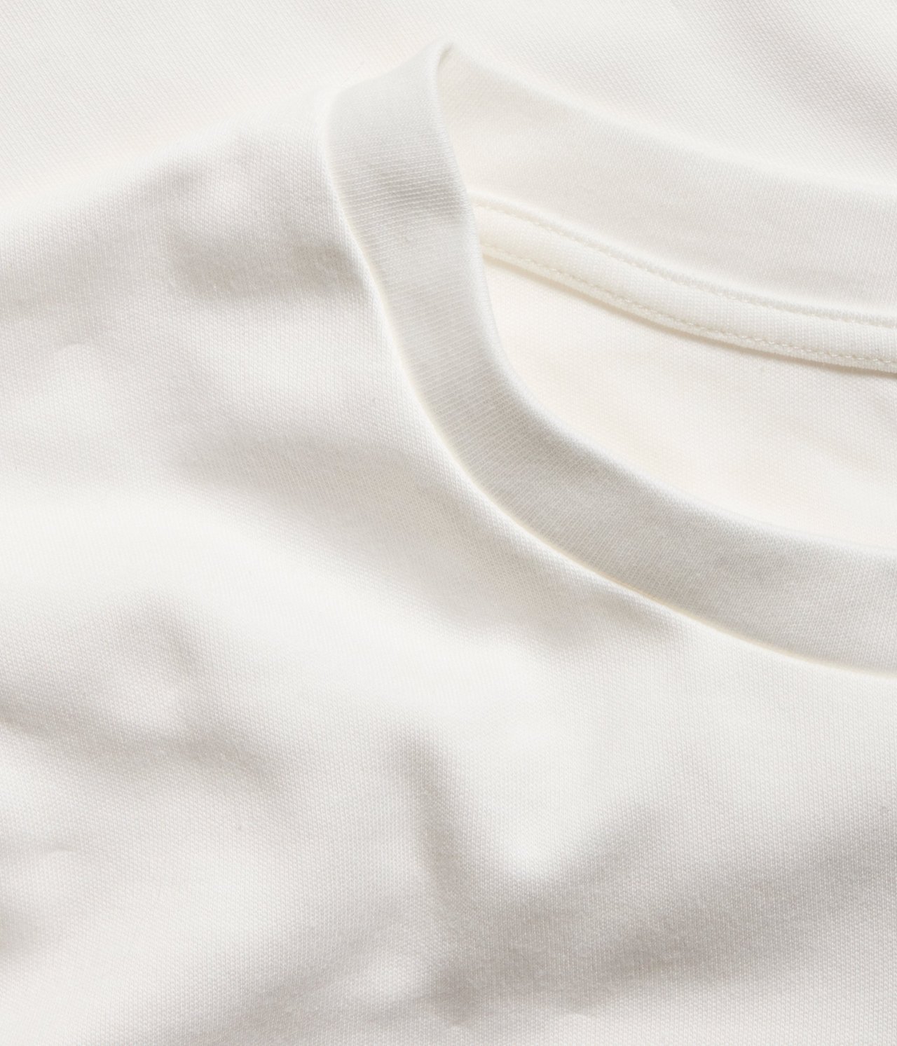 Zbliżenie na krótki, jednolity T-shirt bawełniany w kolorze ecru z prążkowanym dekoltem.