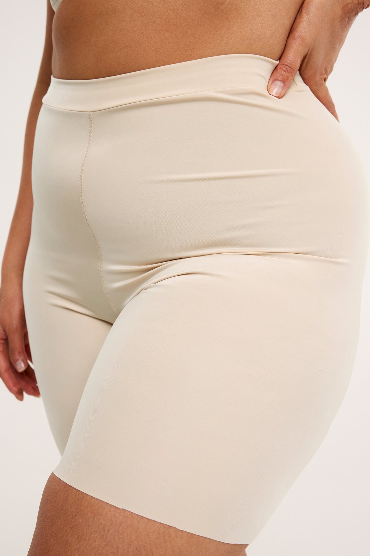 Nærbilde sidevisning av en kvinne i beige shaping-shorts i mykt, elastisk mikrostoff.