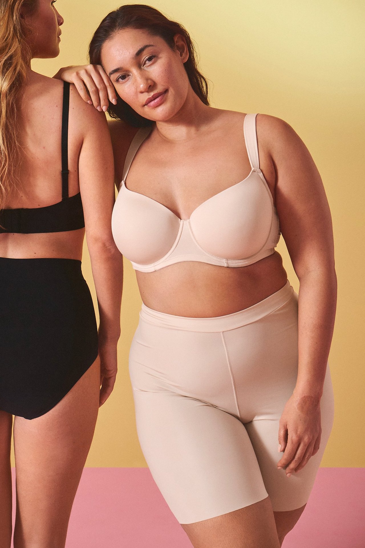 Forfra: kvinne i beige shaping-shorts og BH. En annen kvinne har på seg svarte truser.