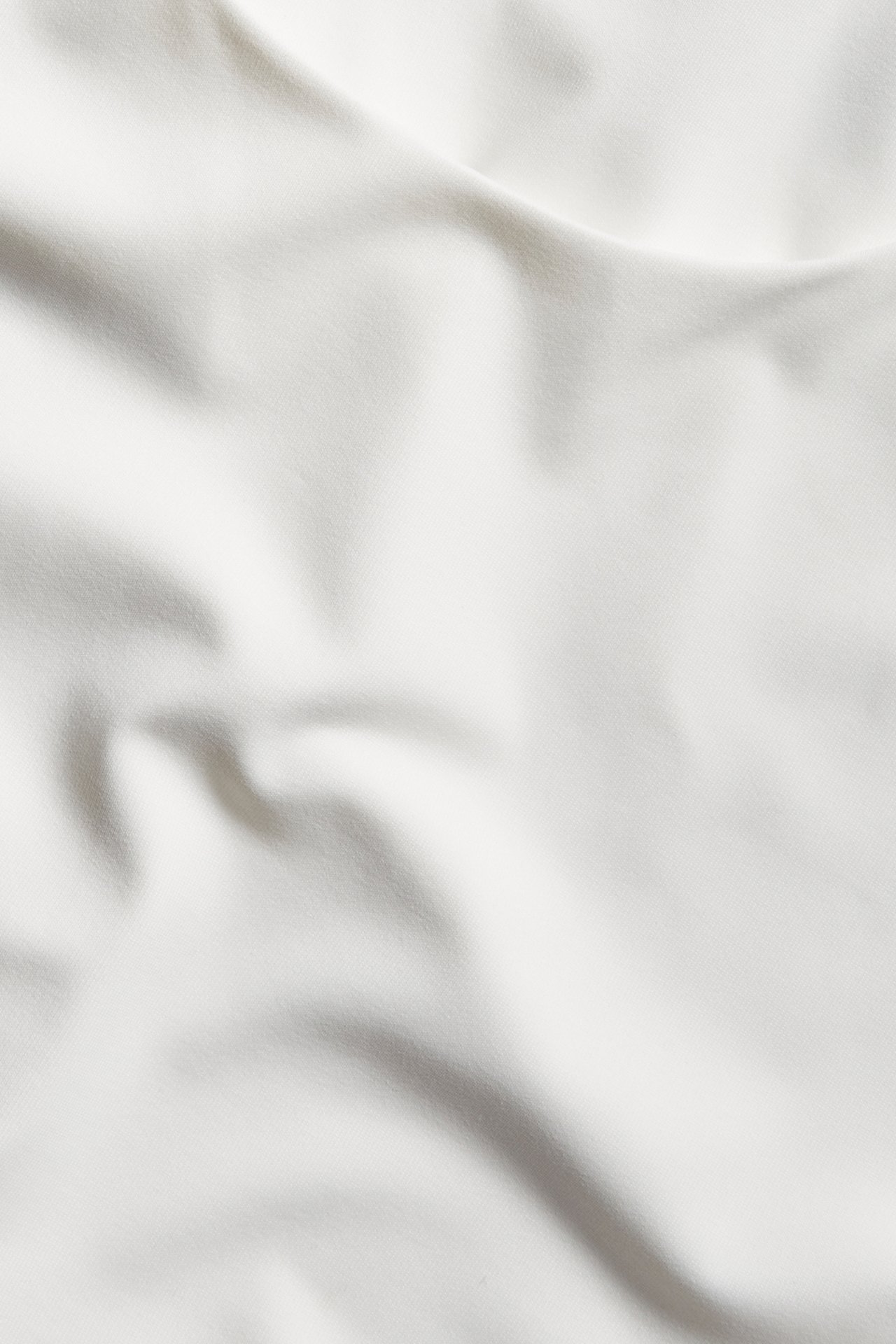 Nærbilde av et ensfarget offwhite polyamid-elastan stoff med myke folder, for en tettsittende topp.