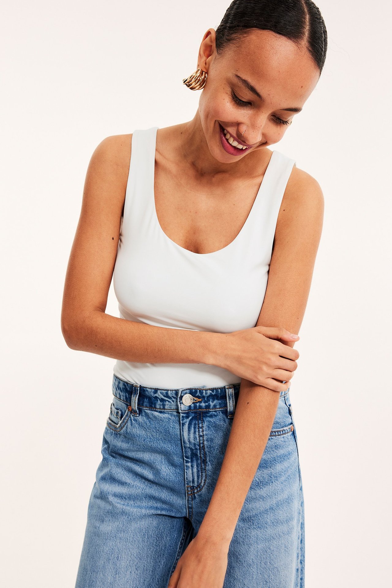 Frontvisning av en kvinne i offwhite stramt linne, blå jeans og gullfargede øreringer.