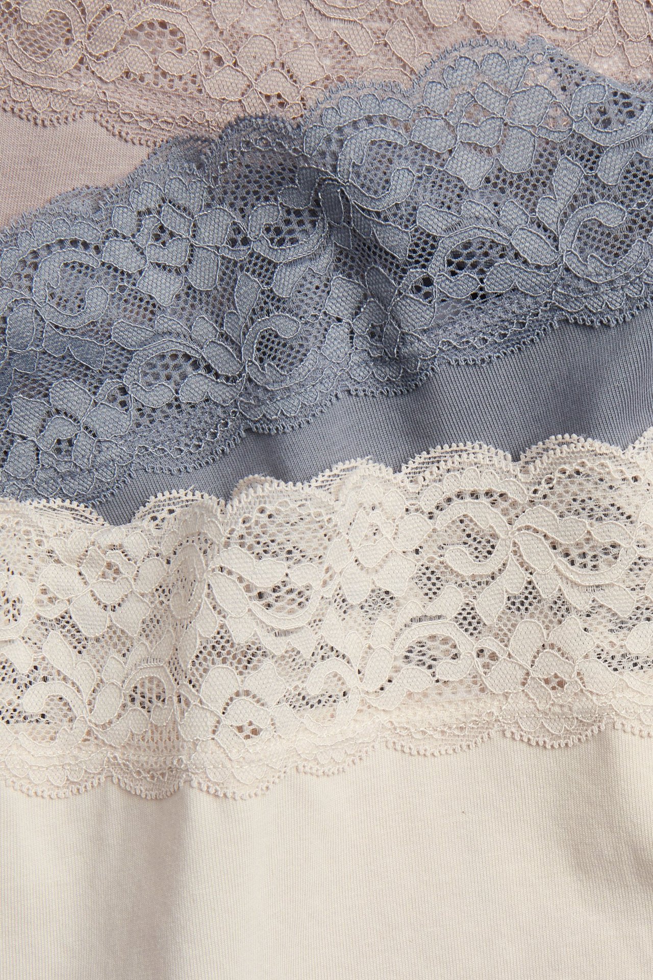 Zbliżenie na trzy bawełniane figi typu hipster z koronkowym pasem: jasnoróżowe, szaroniebieskie i kremowe.