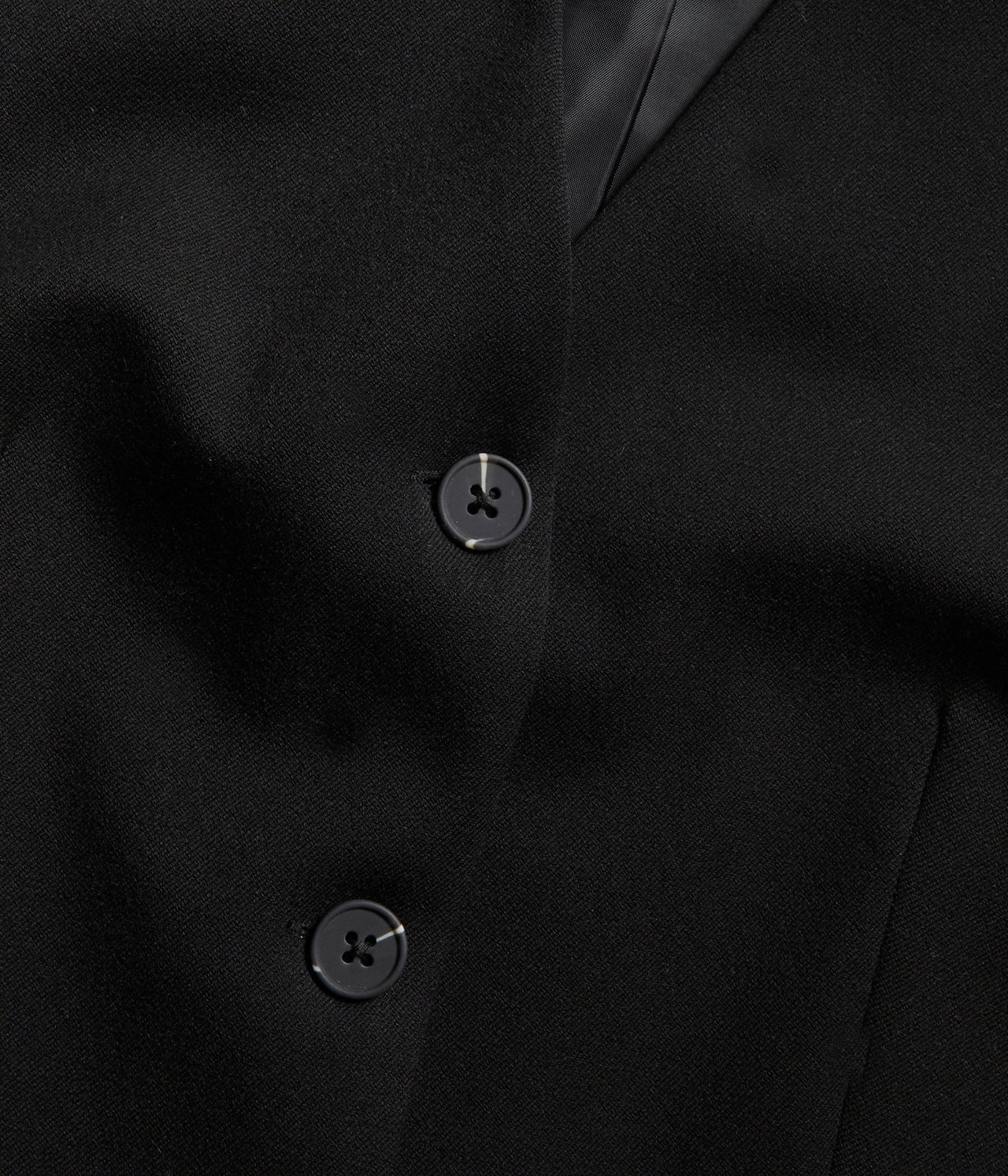 Zbliżenie czarnej kamizelki z dwoma ciemnymi guzikami.