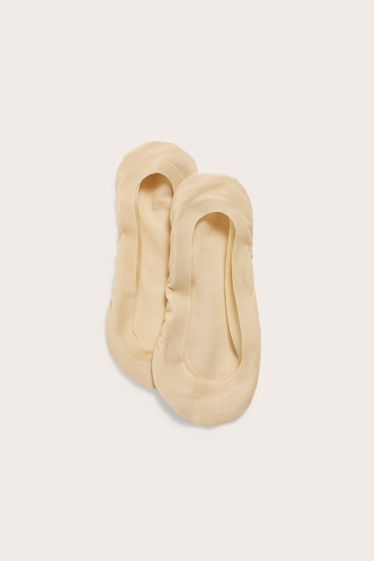 Topputsikt av to lys beige ensfargede footsies i glatt tekstil, lavt skåret med silikonkant.