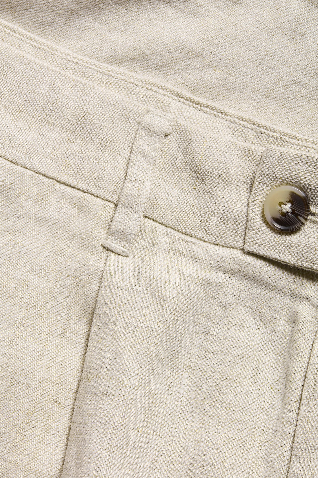 Närbild av beiga linneshorts, som visar det texturerade tyget, en bälteshälla och en ljusbrun knapp.