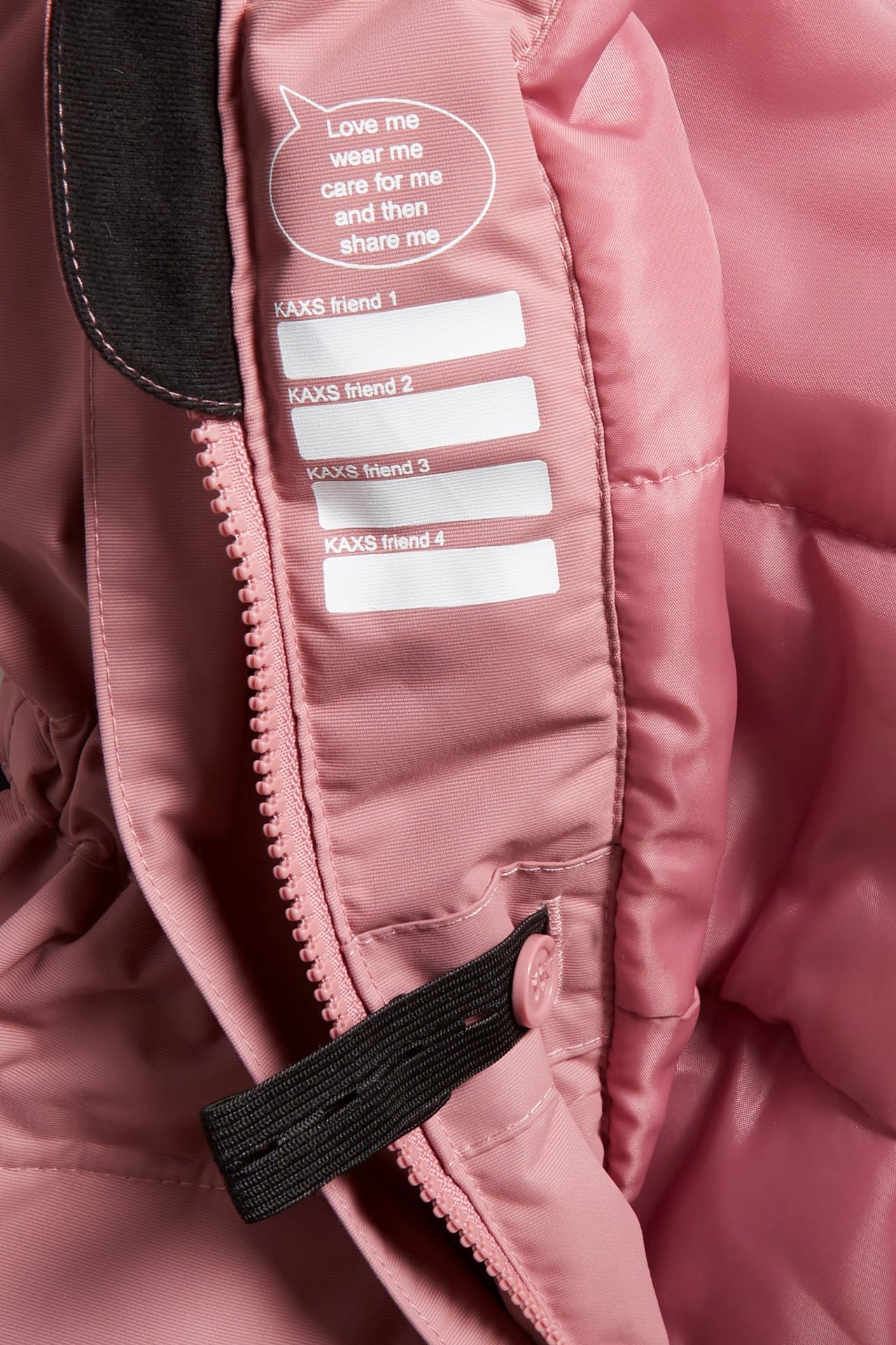 Närbild på en rosa vadderad vinteroveralls innerfoder, visar dragkedja, knapp och en vit etikett.