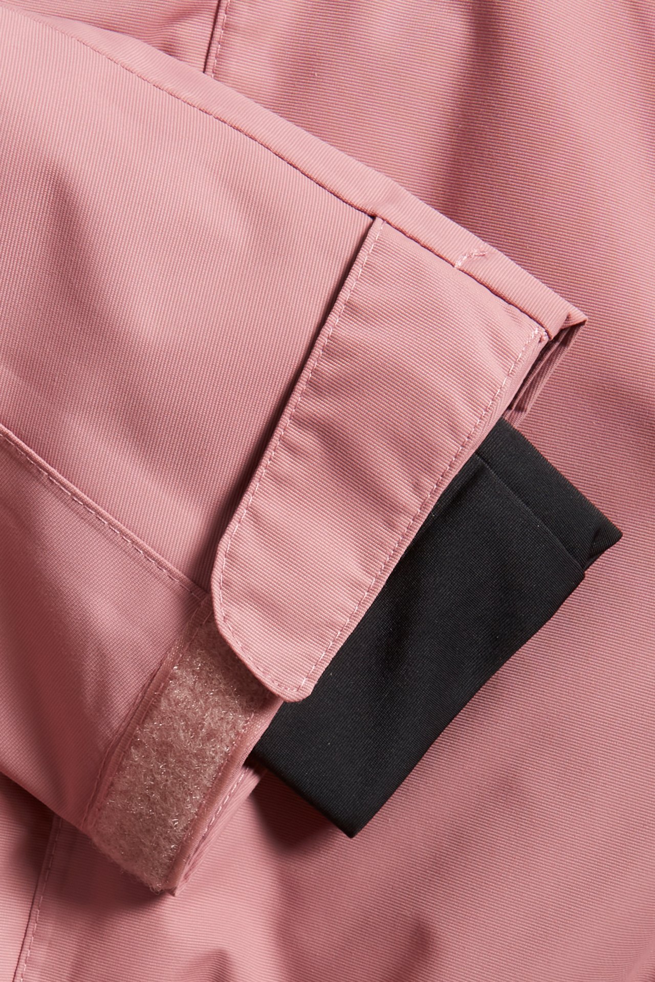 Närbild av en rosa vinteroverallärm med svart innermudd och justerbart rosa kardborreband.