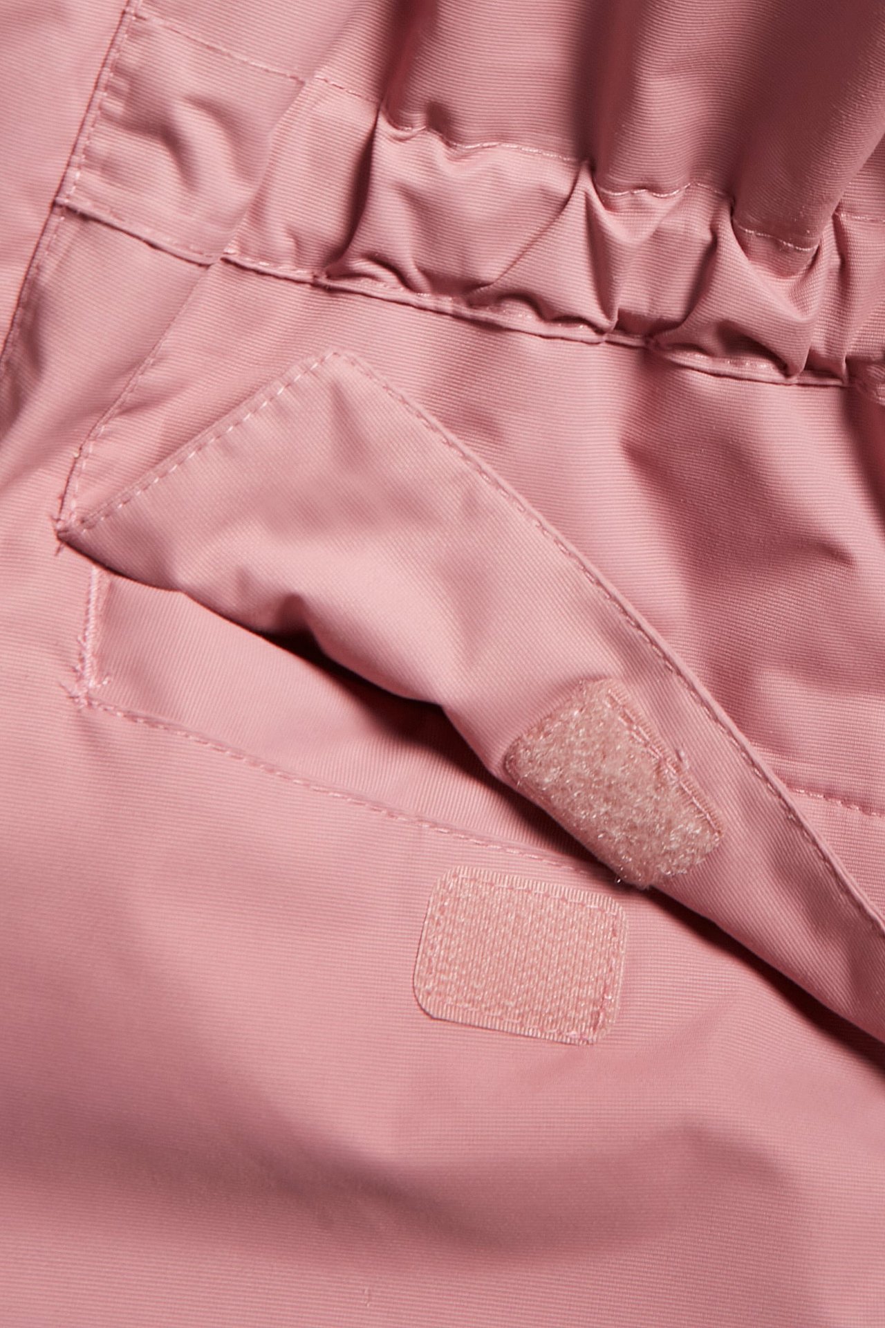 Närbild av en rosa barnvinteroverall, visar ficklock med kardborreknäppning och elastisk midja.